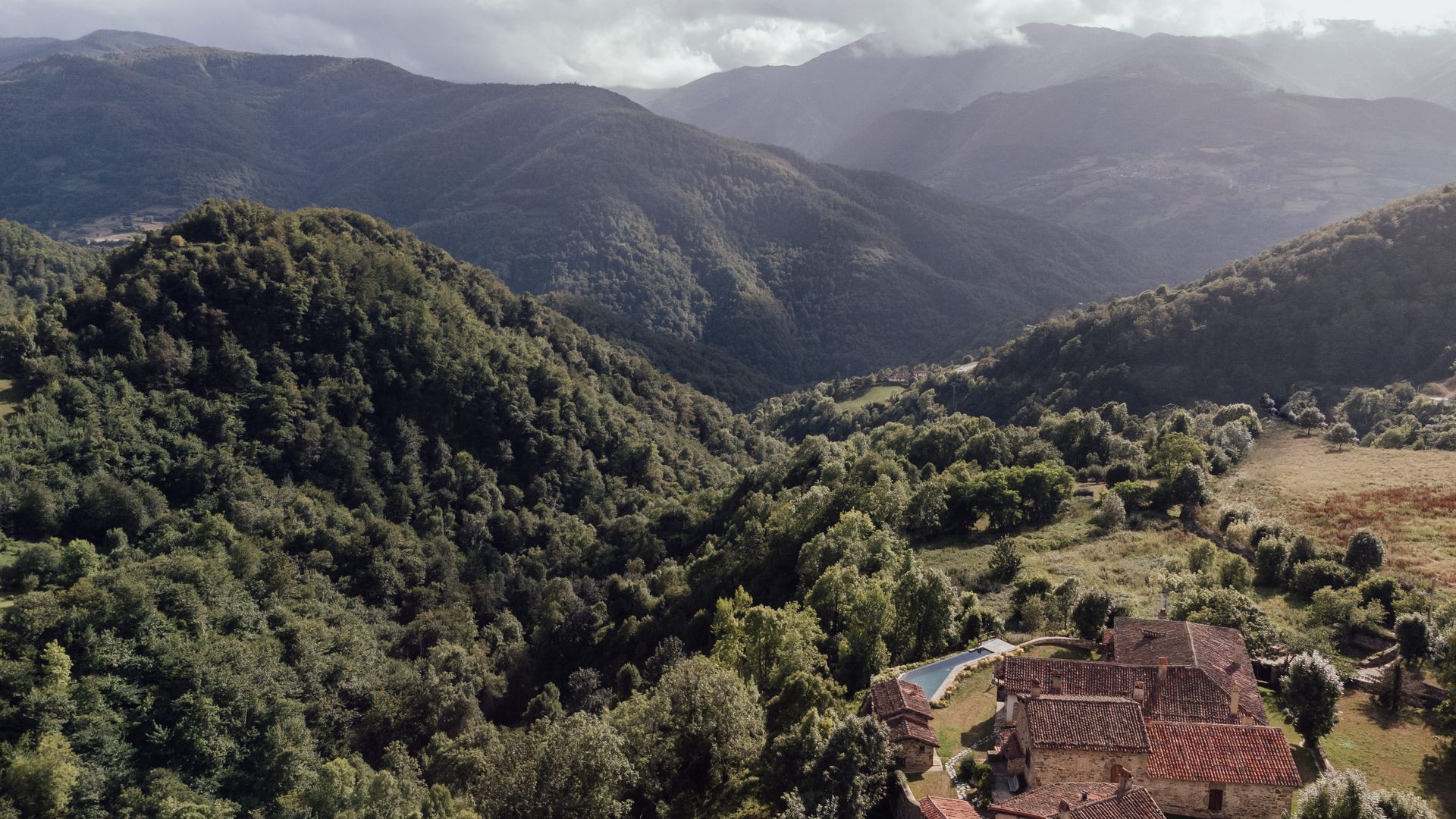 Rolling green hills and mountains, with a building and pool at the bottom.
