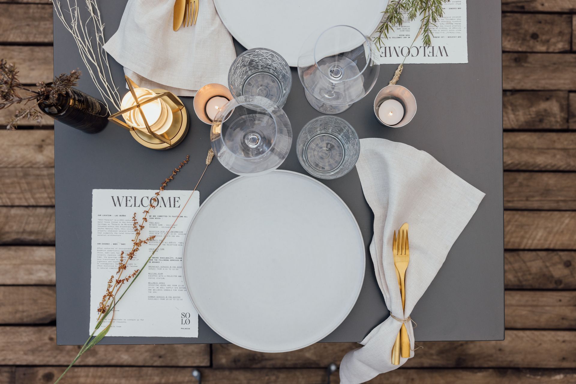 Overhead view of a table setting. White plates, glasses, and gold utensils on a gray surface