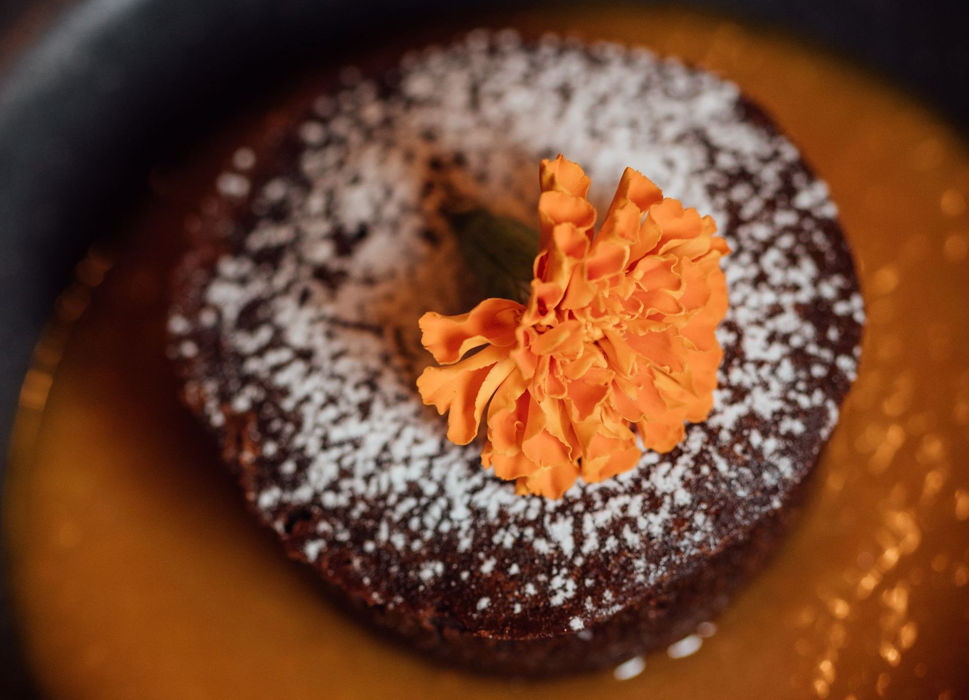 Chocolate lava cake with powdered sugar, orange flower, and sauce.