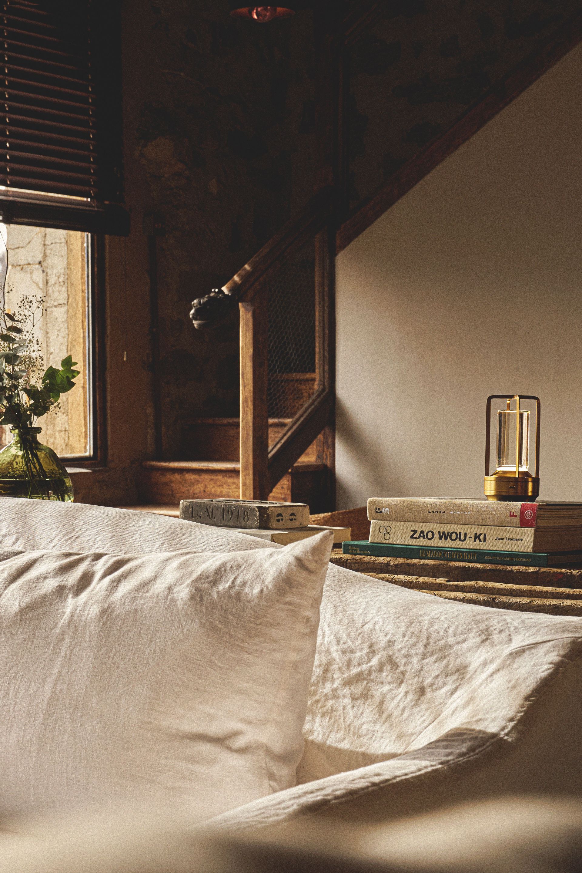 Cozy interior with a window, books, and lamp on a wooden table. Sunlight streams in, illuminating the space.