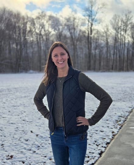 Woman smiling outdoors in winter, standing on a snowy path with hands on hips