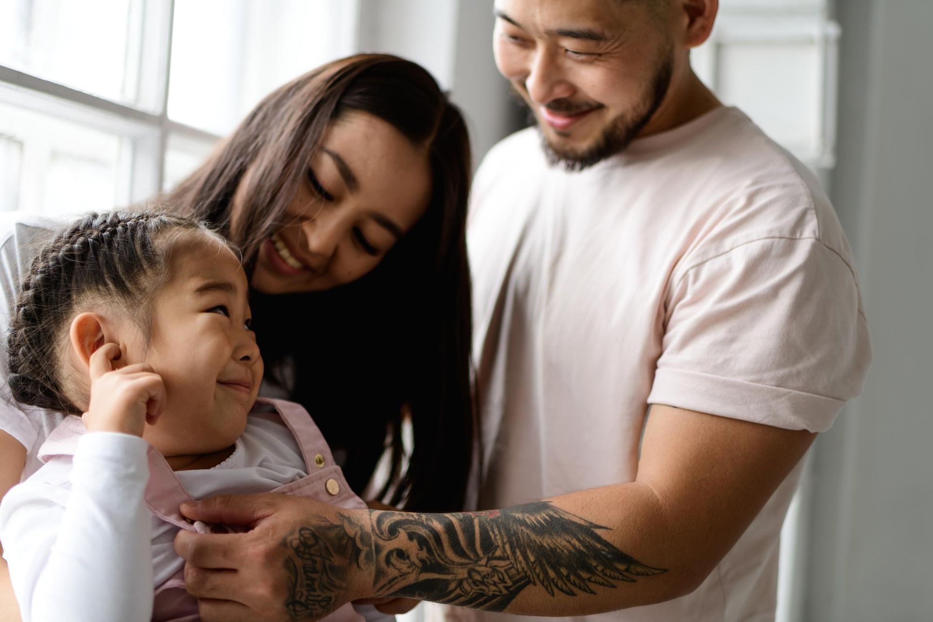 Two adults and a child smiling together indoors, with one adult holding the child’s hand