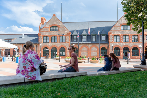 People sitting on a bench in front of a red-brick building on a sunny day.