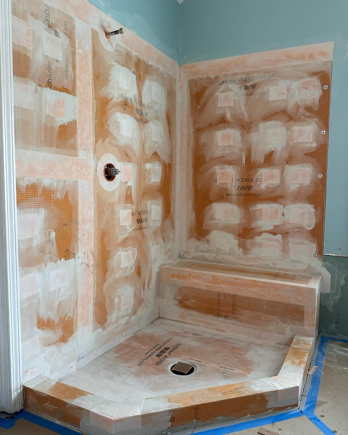 Shower in progress with orange waterproofing membrane and white mortar.