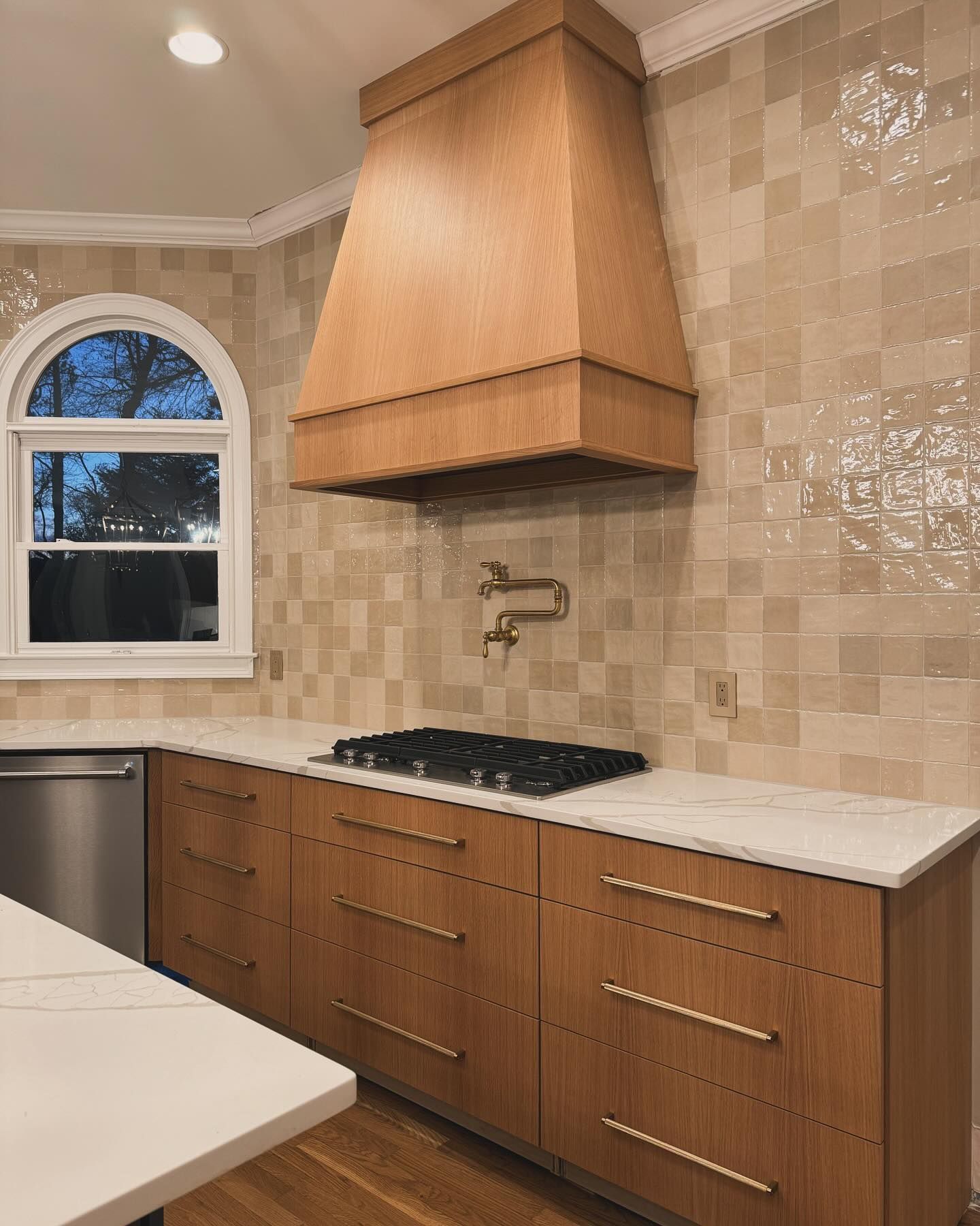 Modern kitchen with wood cabinets, range hood, and tiled backsplash; marble countertops.