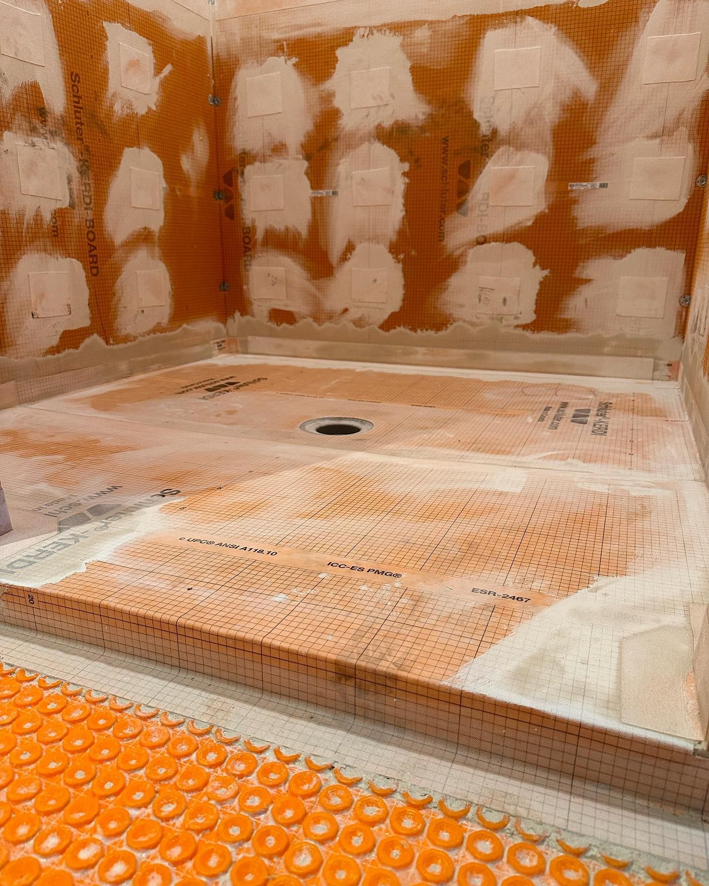 Shower in progress: Orange membrane on floor and walls, with mortar and tile ready for installation.