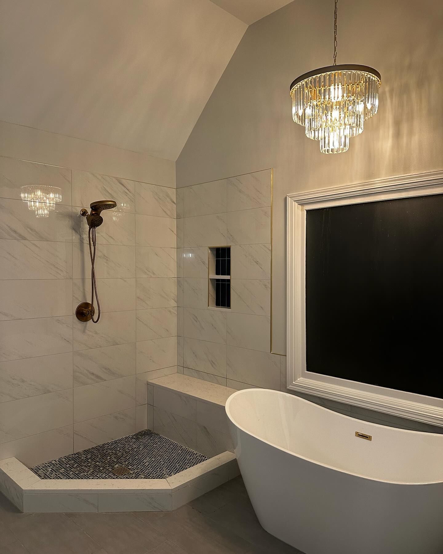 Elegant bathroom: shower with bench and pebble floor, freestanding tub, chandelier, ornate mirror.