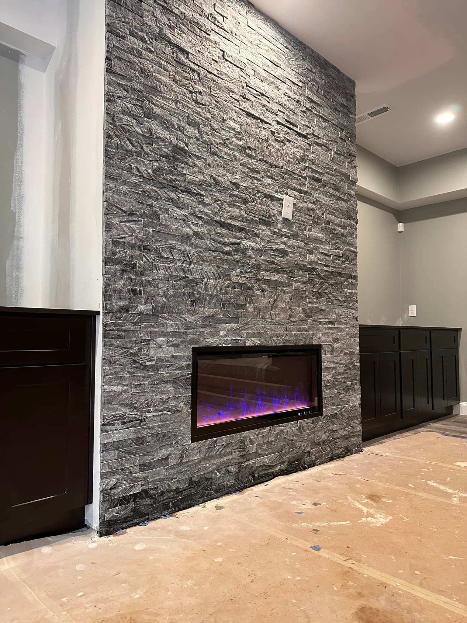 Stone-covered fireplace with electric fire, flanked by dark cabinets, in an unfinished room.