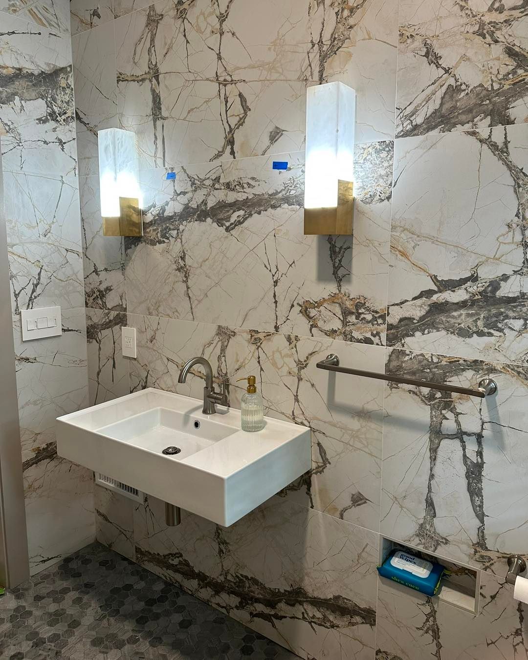 A modern bathroom with a floating sink, marble wall tiles, and two sconce lights.
