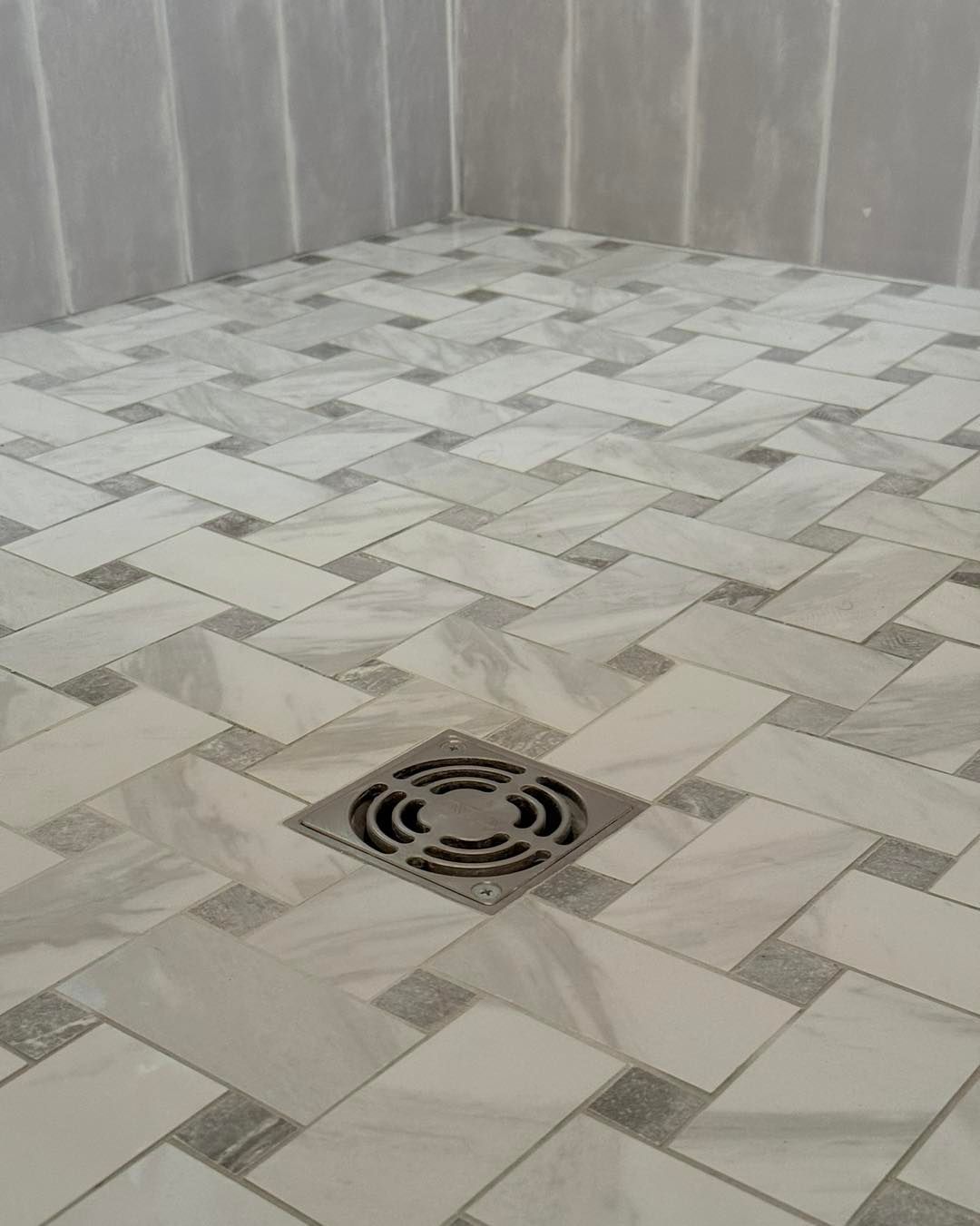 Shower floor with a decorative white and gray tile pattern, featuring a drain.