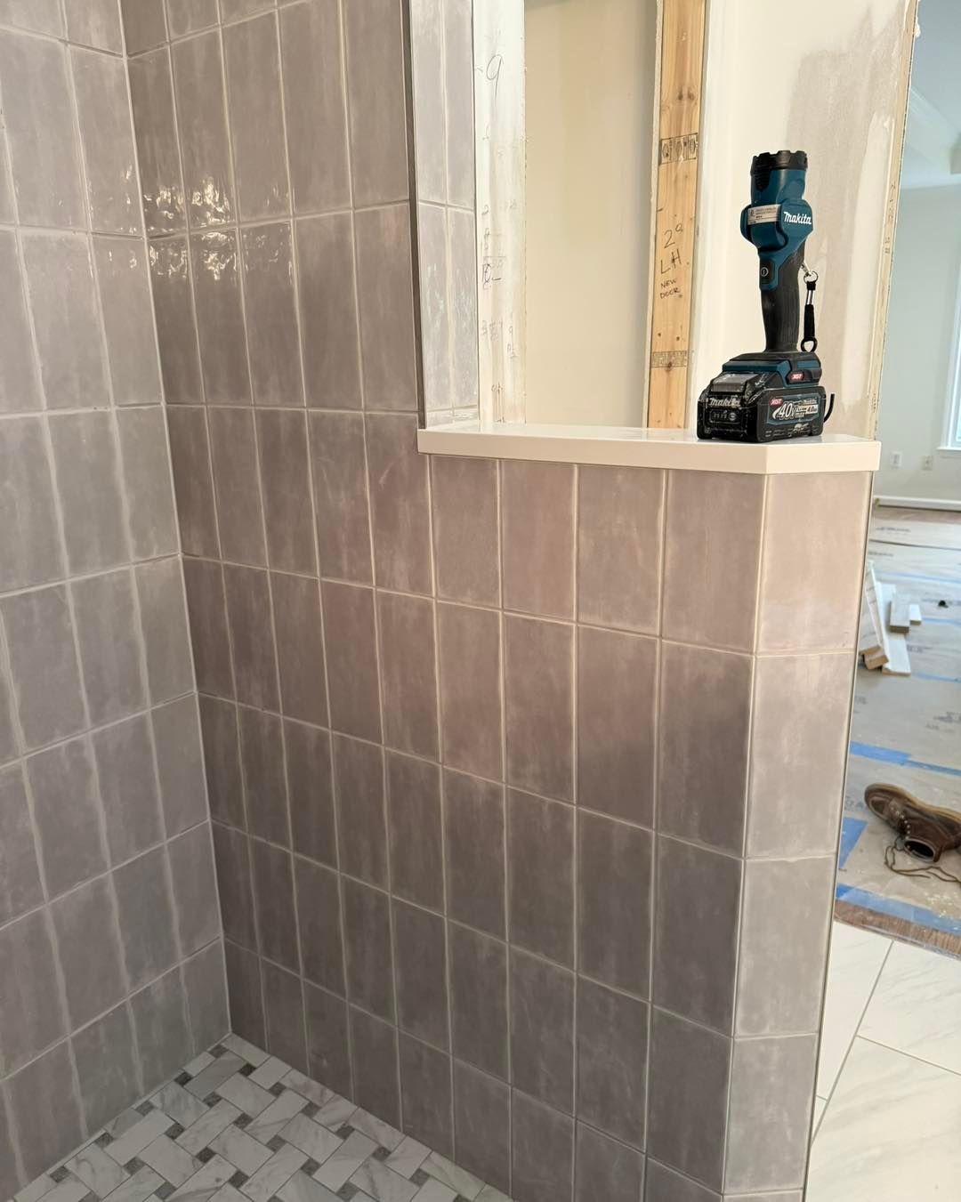 Gray tiled shower with a small shelf under a window; a power drill sits on the shelf.