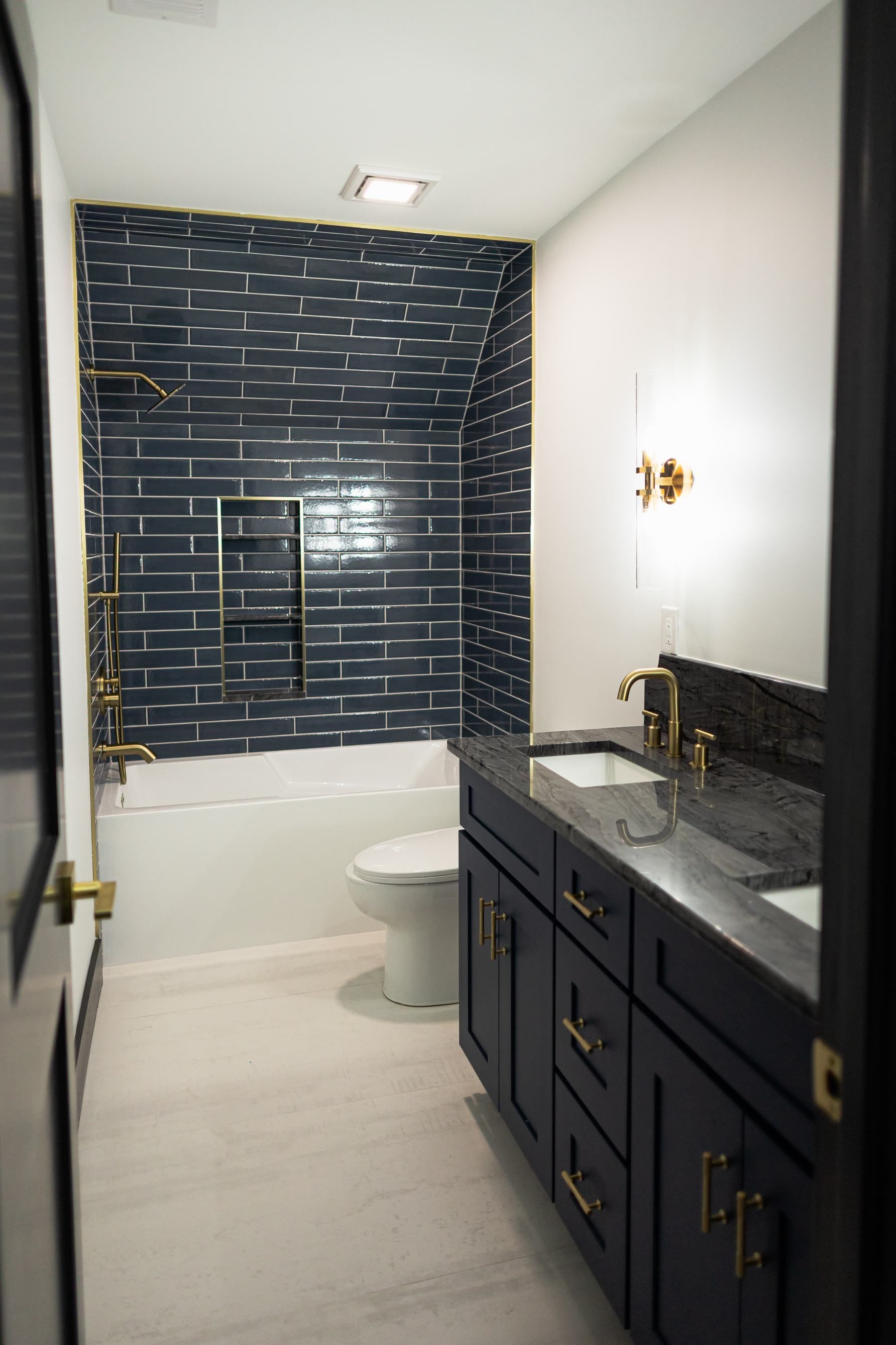Modern bathroom with navy vanity, white walls, and dark blue tiled shower wall.