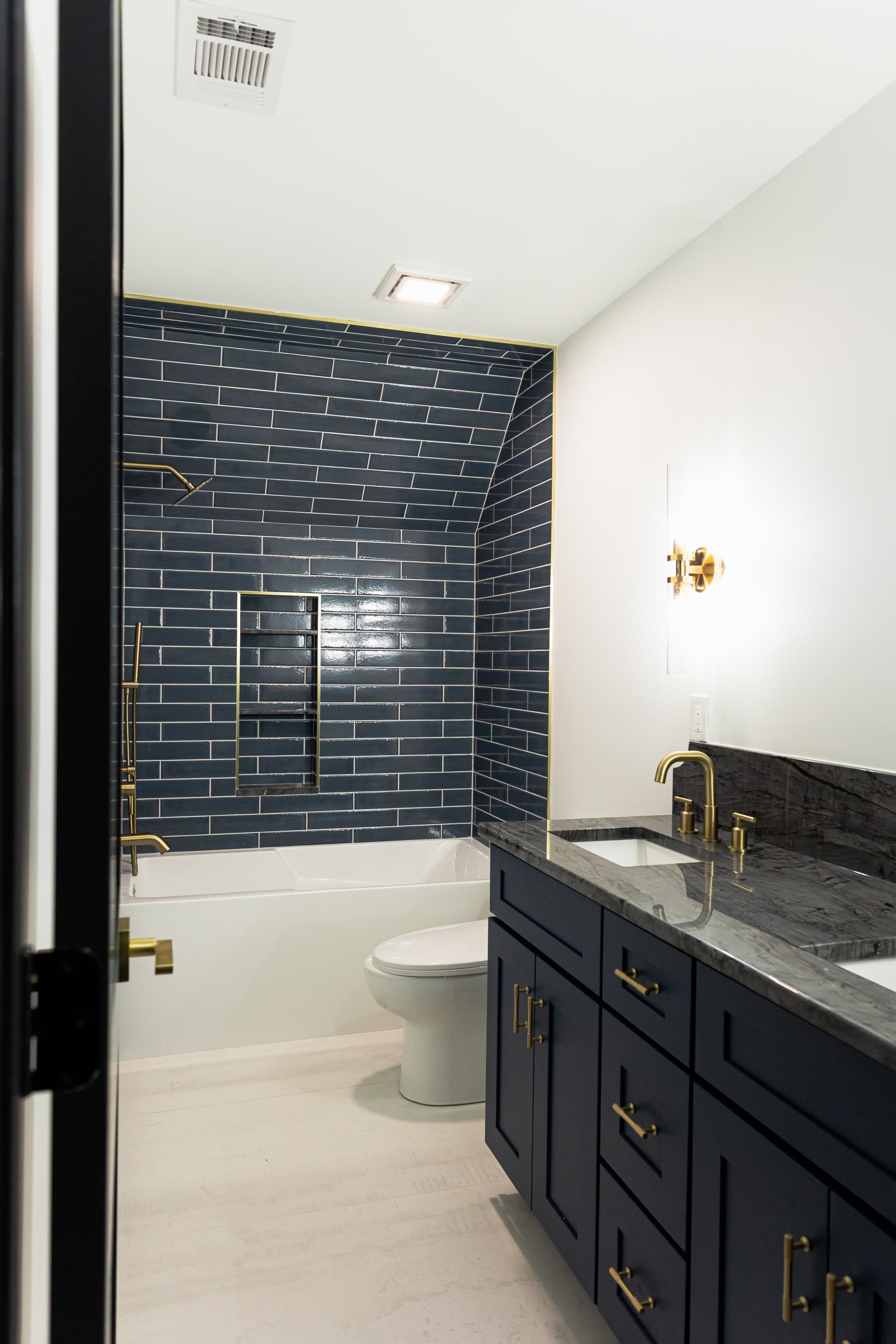 Narrow bathroom with dark navy vanity, black tile shower wall, and white toilet and walls
