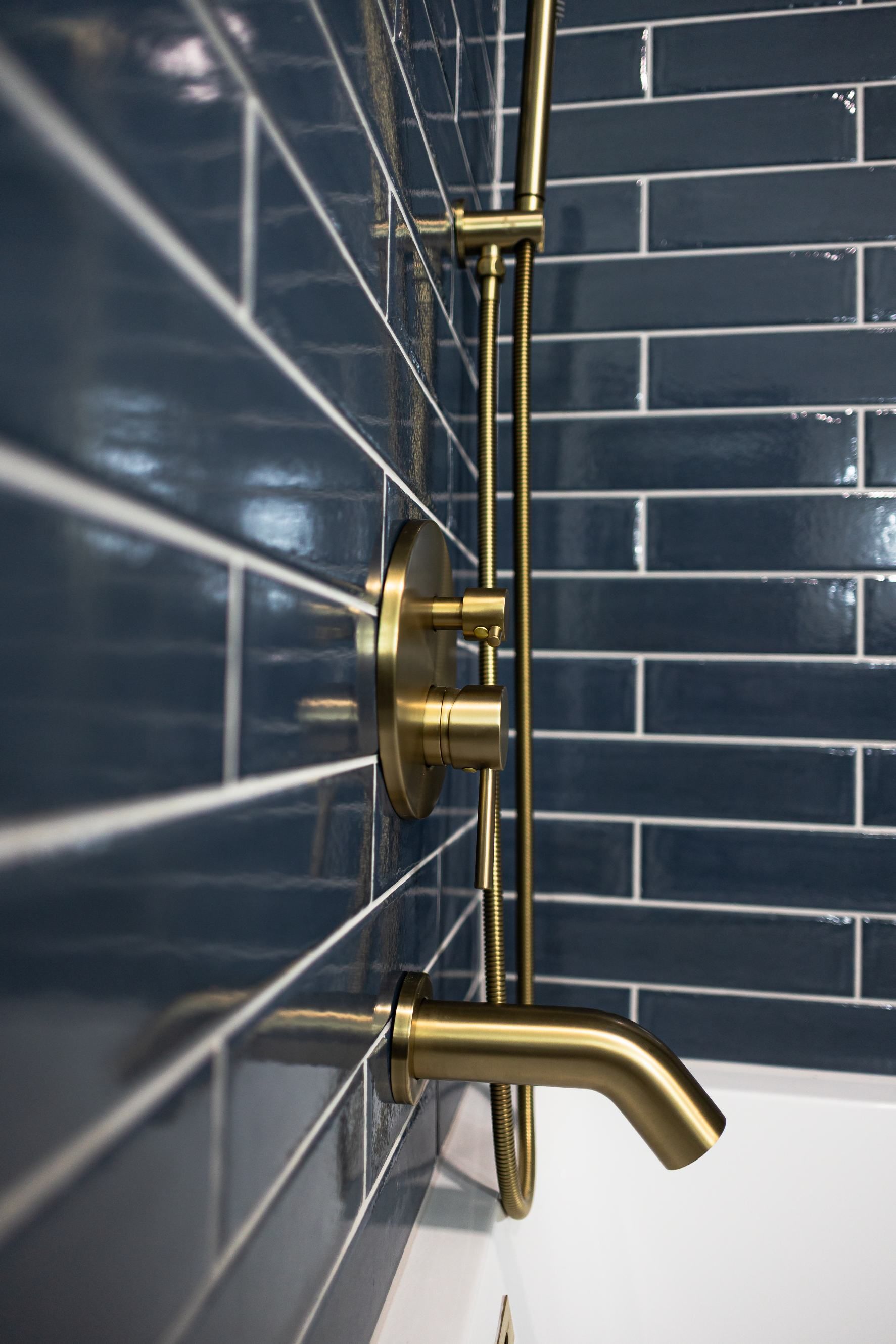 Brass shower fixture on a dark blue tiled bathroom wall with a white bathtub edge visible