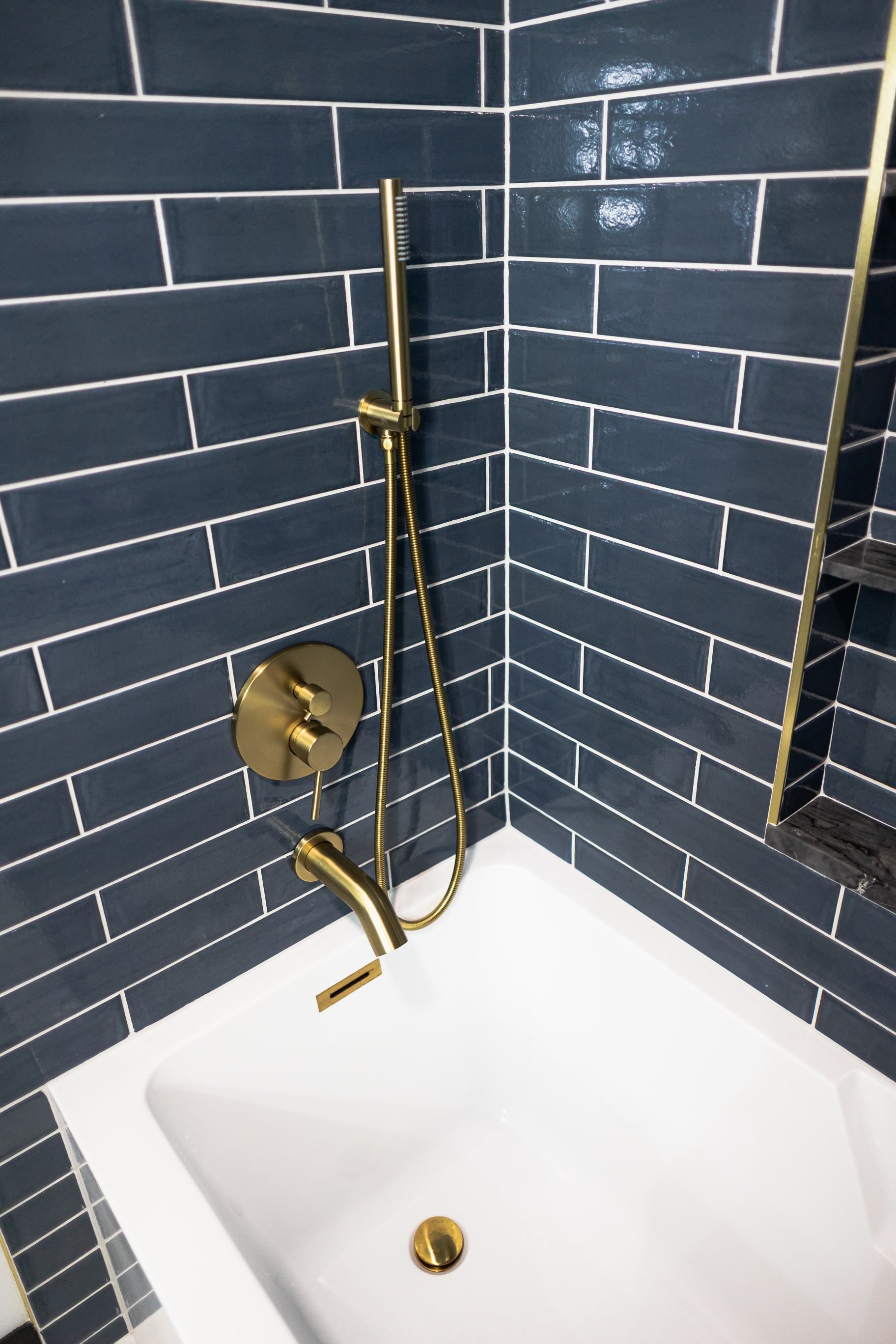 Blue-tiled shower and bathtub with gold fixtures and handheld showerhead.