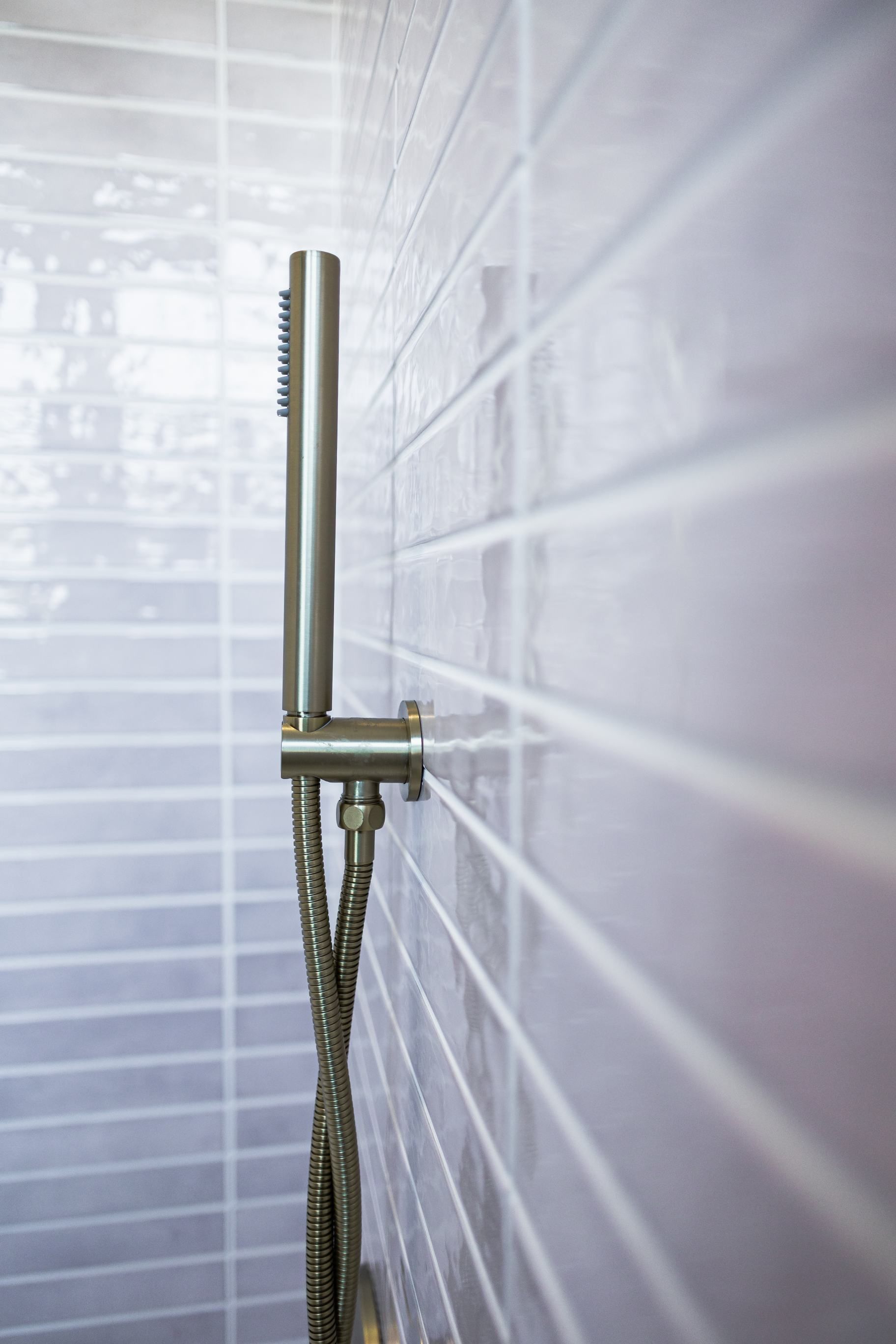 Stainless steel shower fixture with handheld sprayer against white tiled wall and window blinds