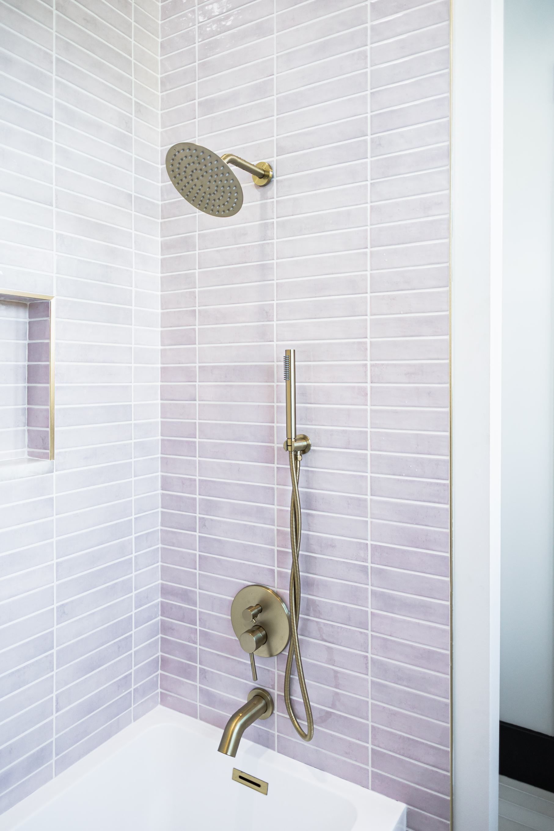 Modern shower with white tile, chrome handheld showerhead, and built-in soap niche