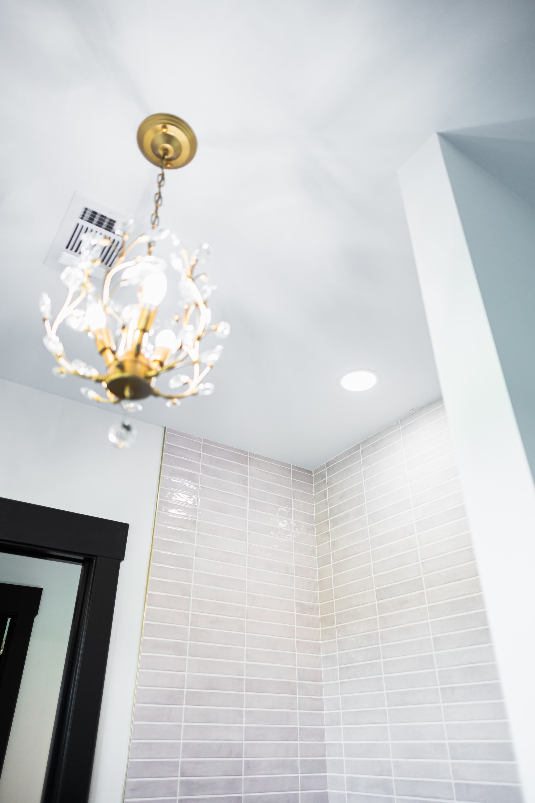 Chandelier hanging from a white ceiling in a bright tiled room corner