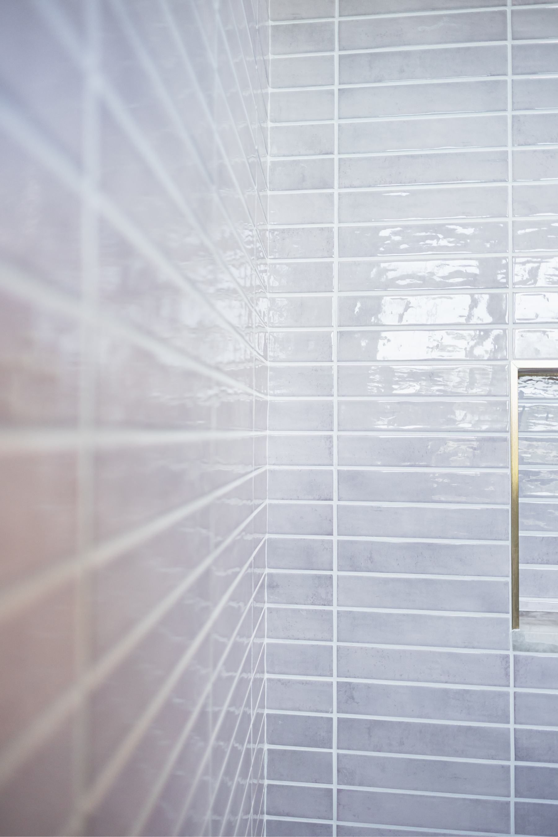 Close-up of glossy white tiled bathroom wall with a yellow shower edge on the right