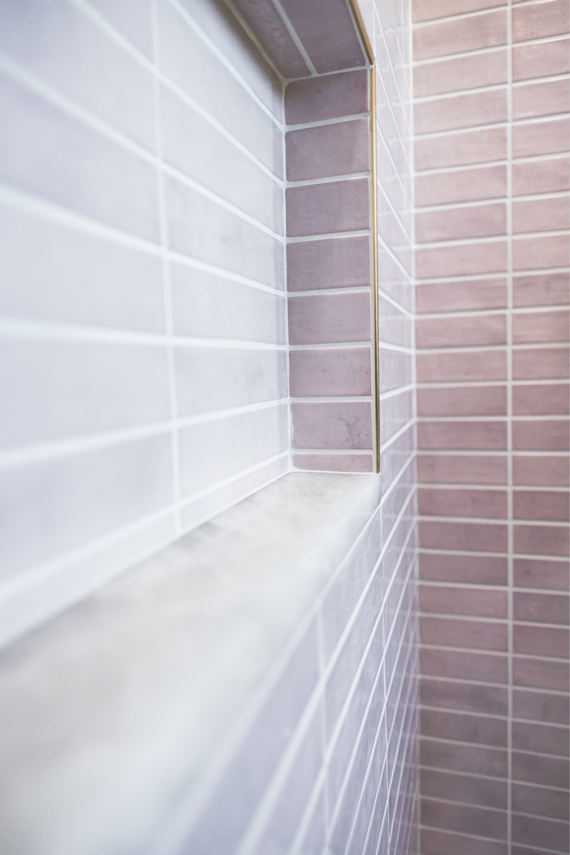 Narrow tiled shower corner with white and mauve tiles and a marble ledge