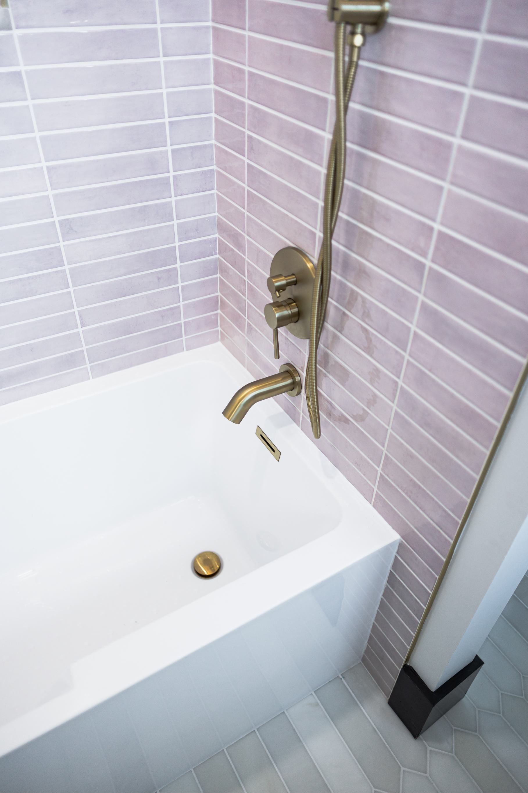 Bathtub with brass shower faucet and handheld sprayer against pink tile walls