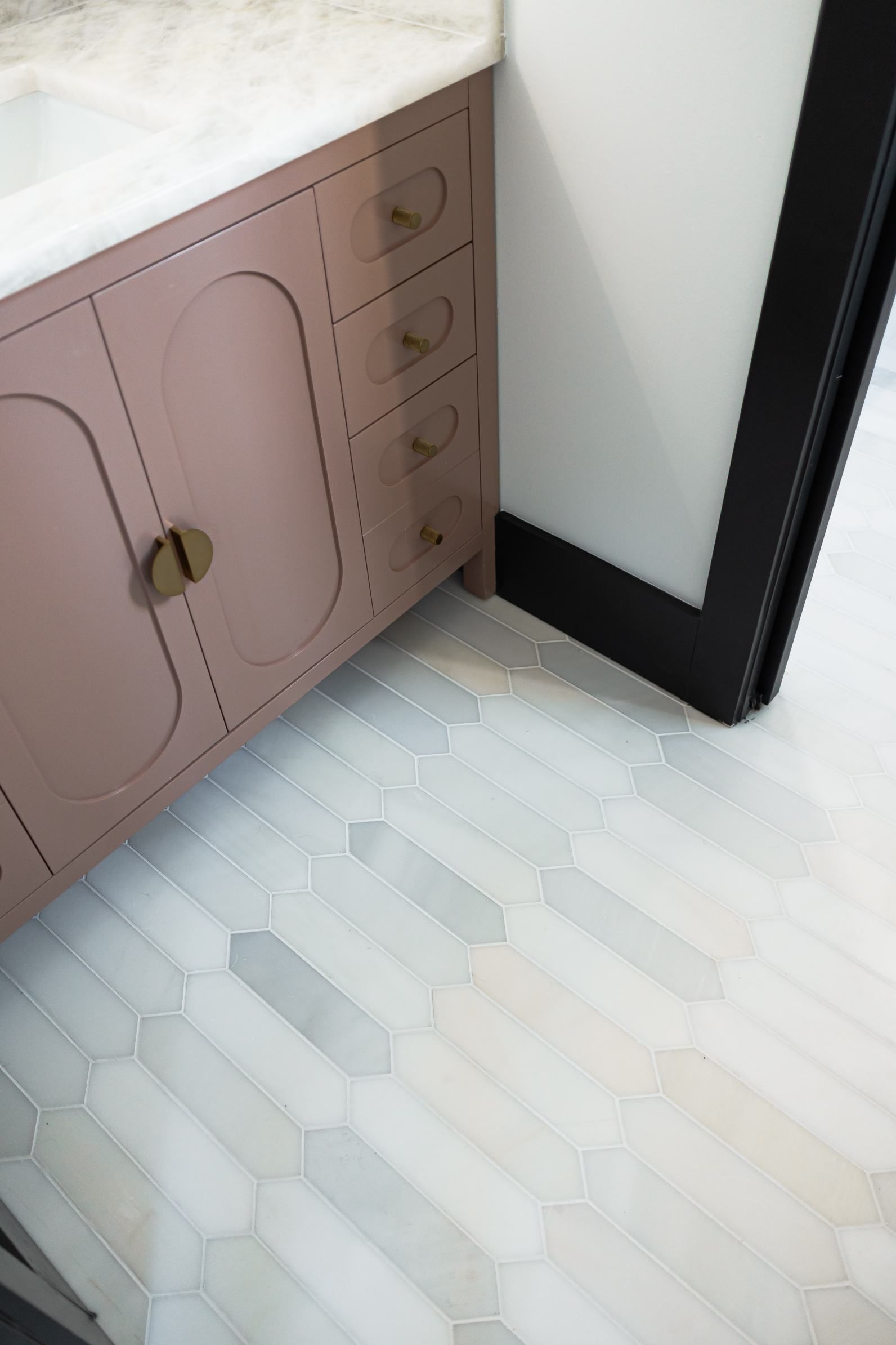 Pink bathroom vanity beside a white wall and black-framed mirror over light patterned tile floor