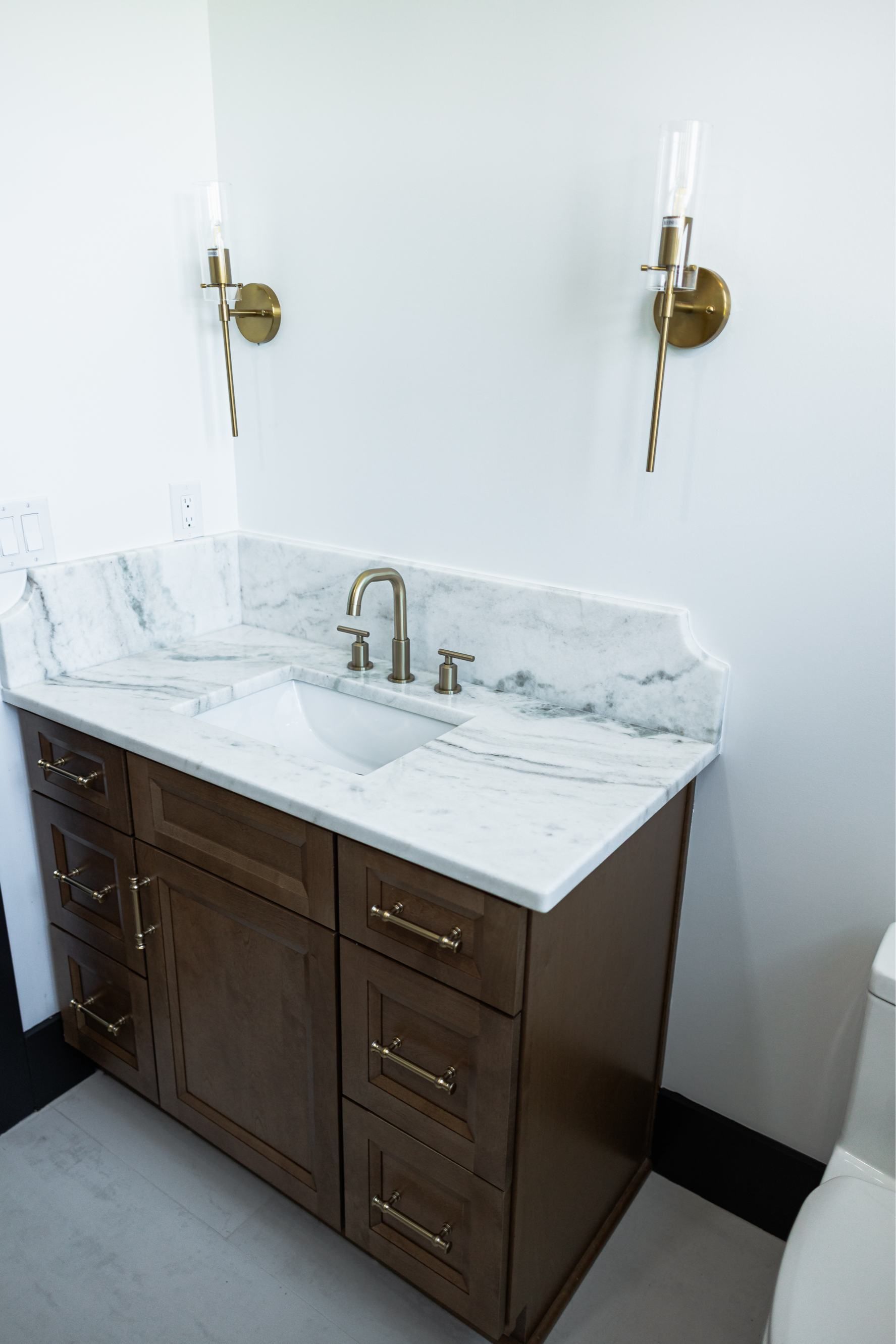 White marble bathroom vanity with brown cabinets, sink, mirror, and wall sconces.