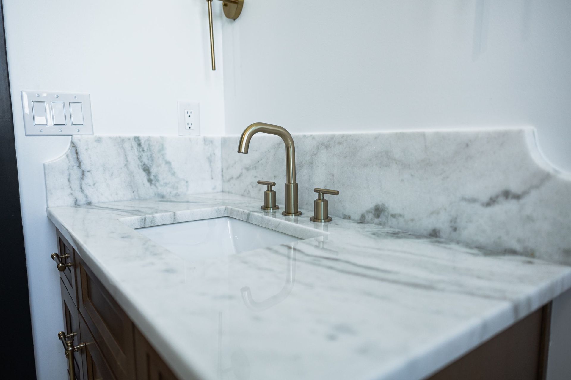 White marble bathroom vanity with brass faucet and matching backsplash tiles