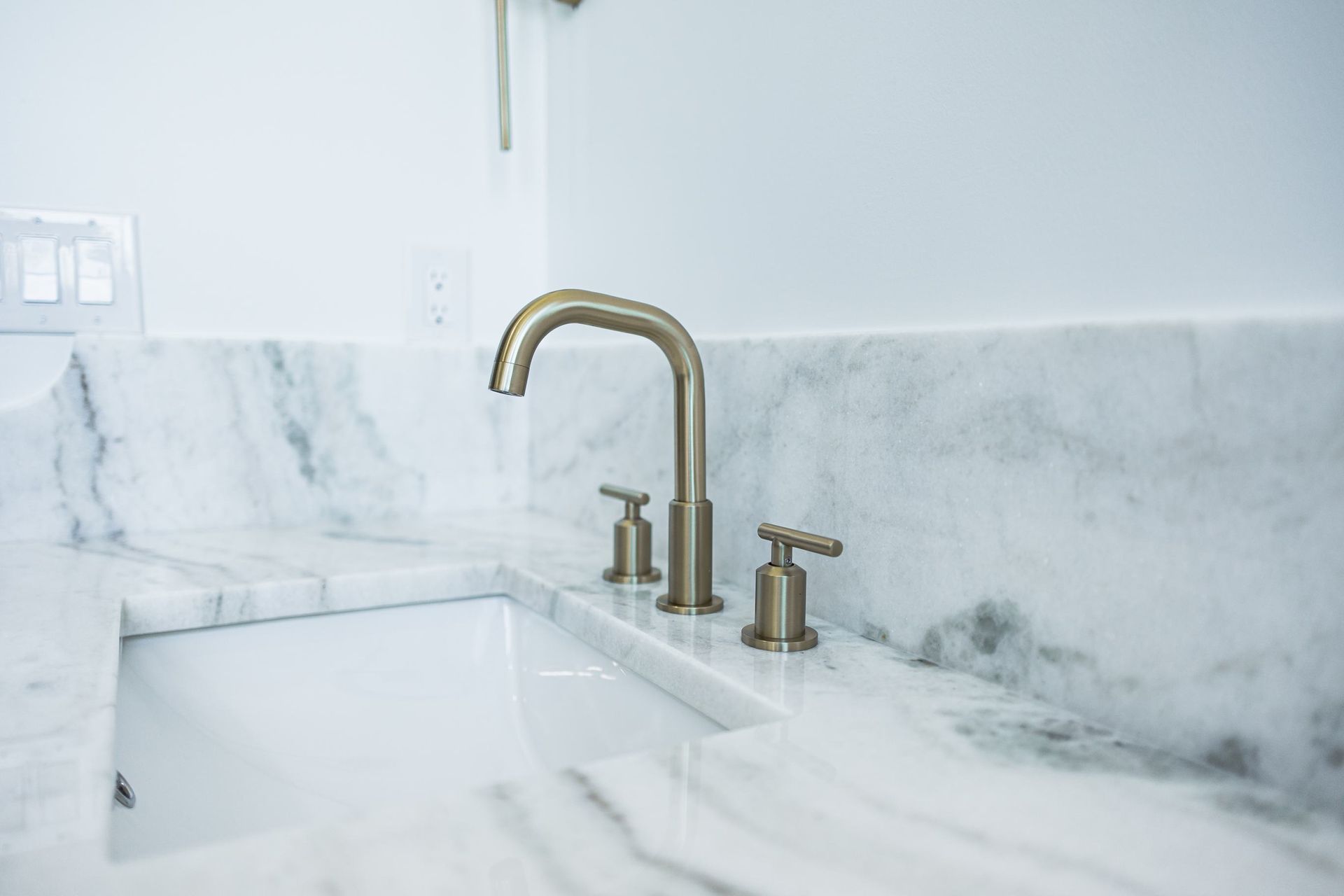 White marble bathroom sink with brass faucet and handles against a marble backsplash
