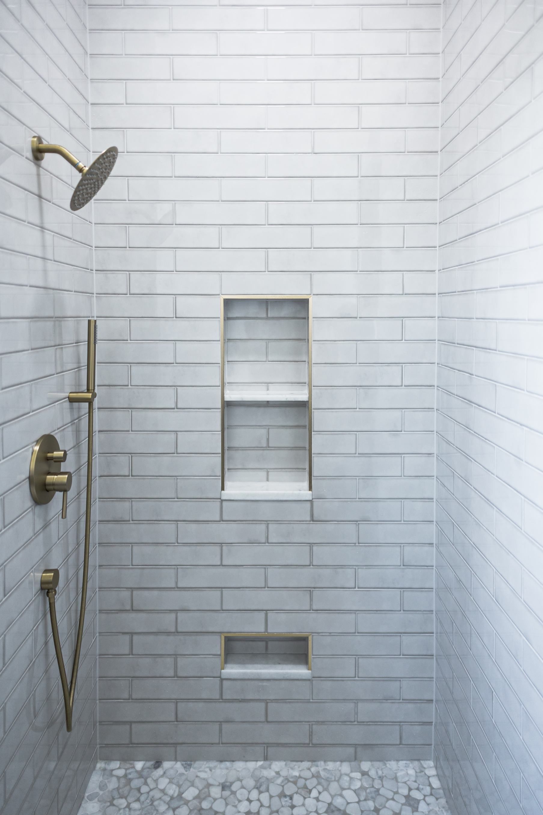 Modern white-tiled shower with built-in niche, shelf, and handheld showerhead on the left.