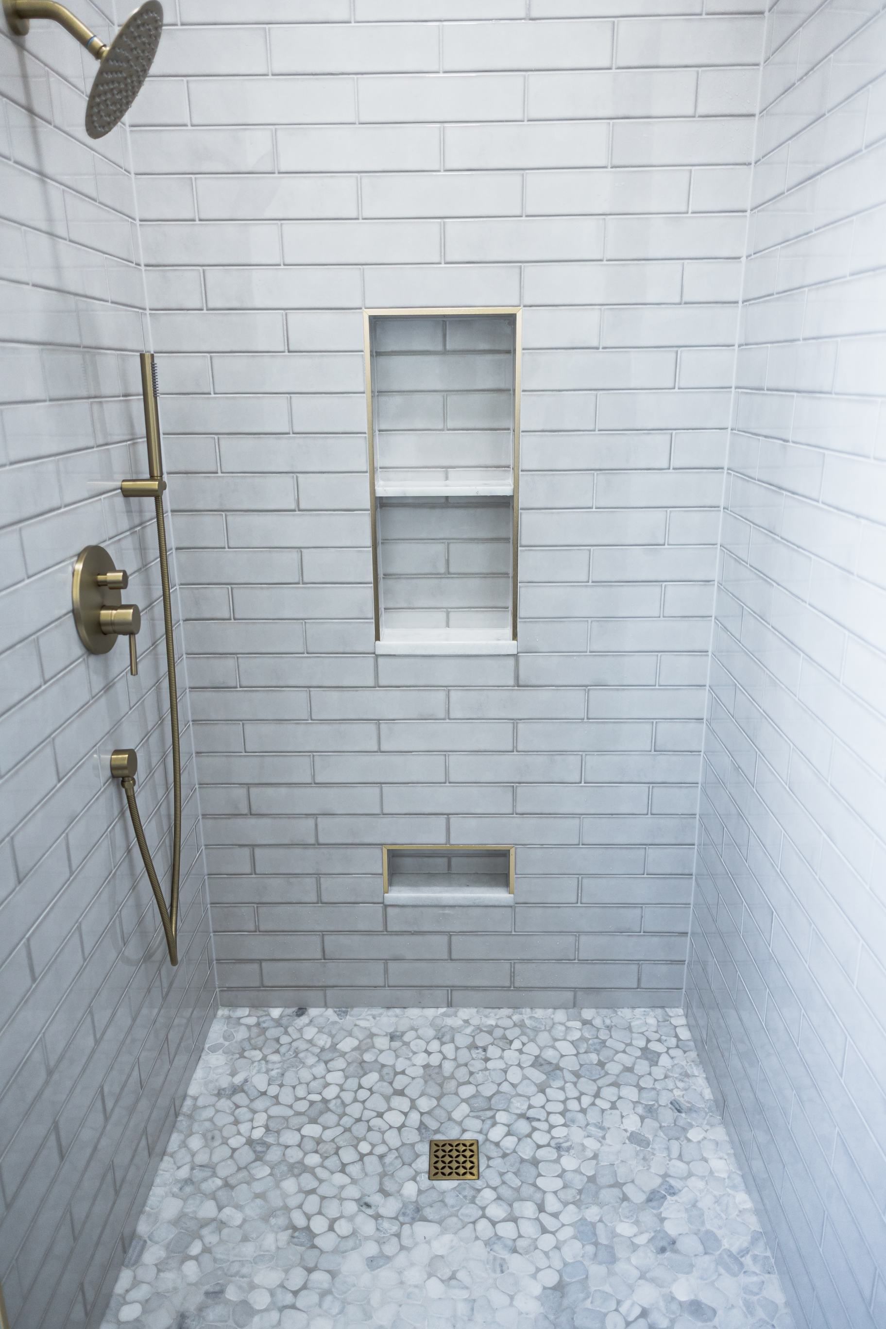 White tiled shower with brass fixtures, built-in niche, and mosaic floor drain.