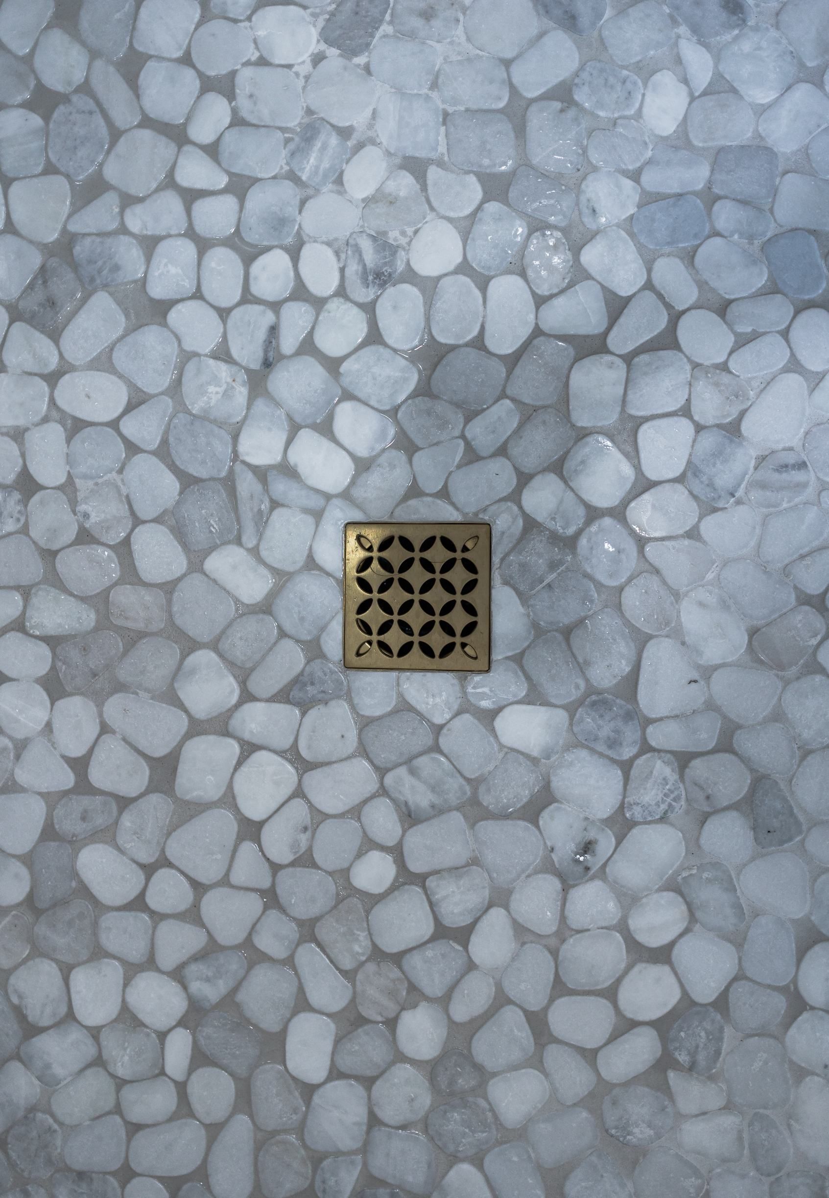 Square drain cover centered on a pale gray pebble-patterned stone surface.