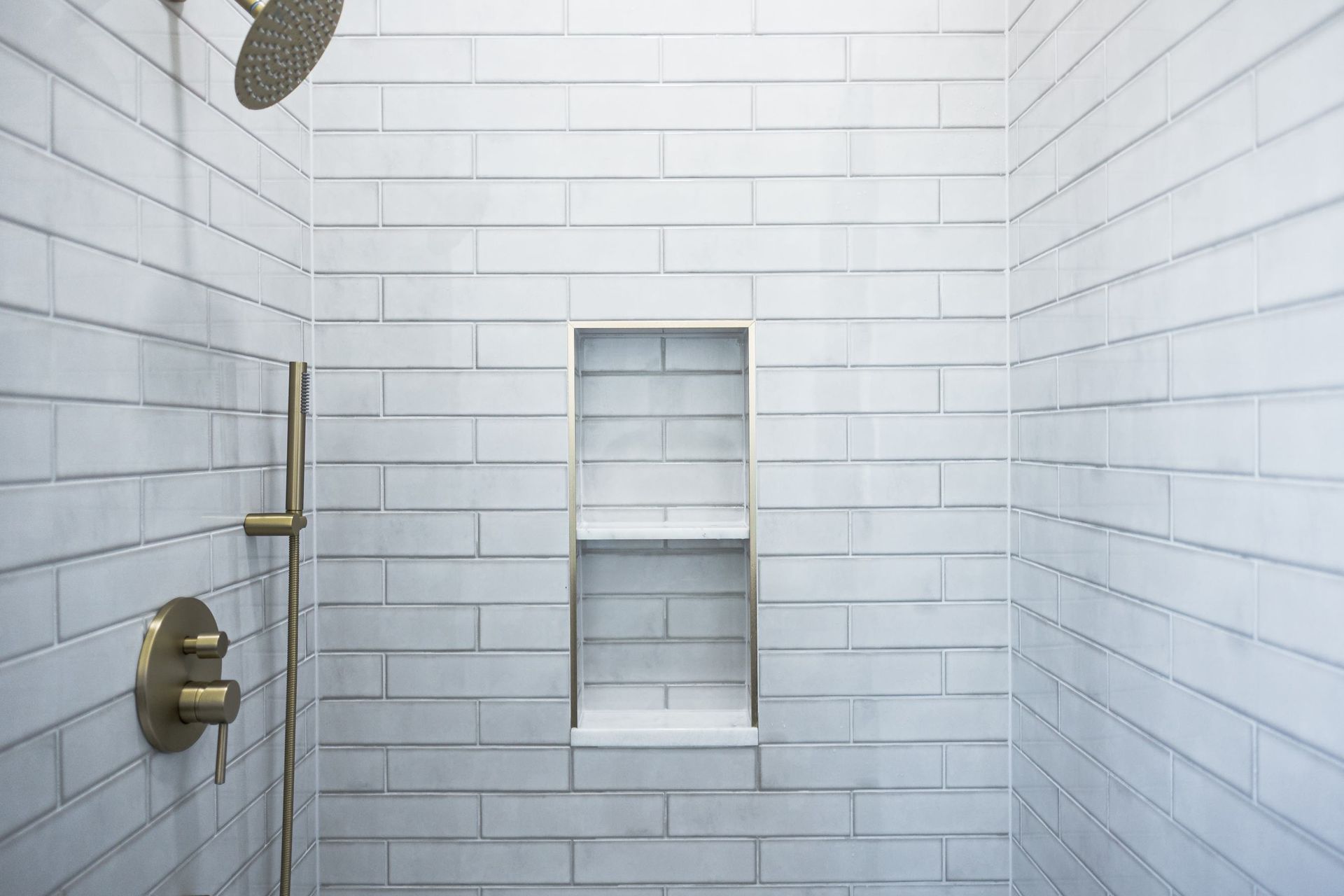 White-tiled shower with built-in niche shelf, brass fixtures, and showerhead visible
