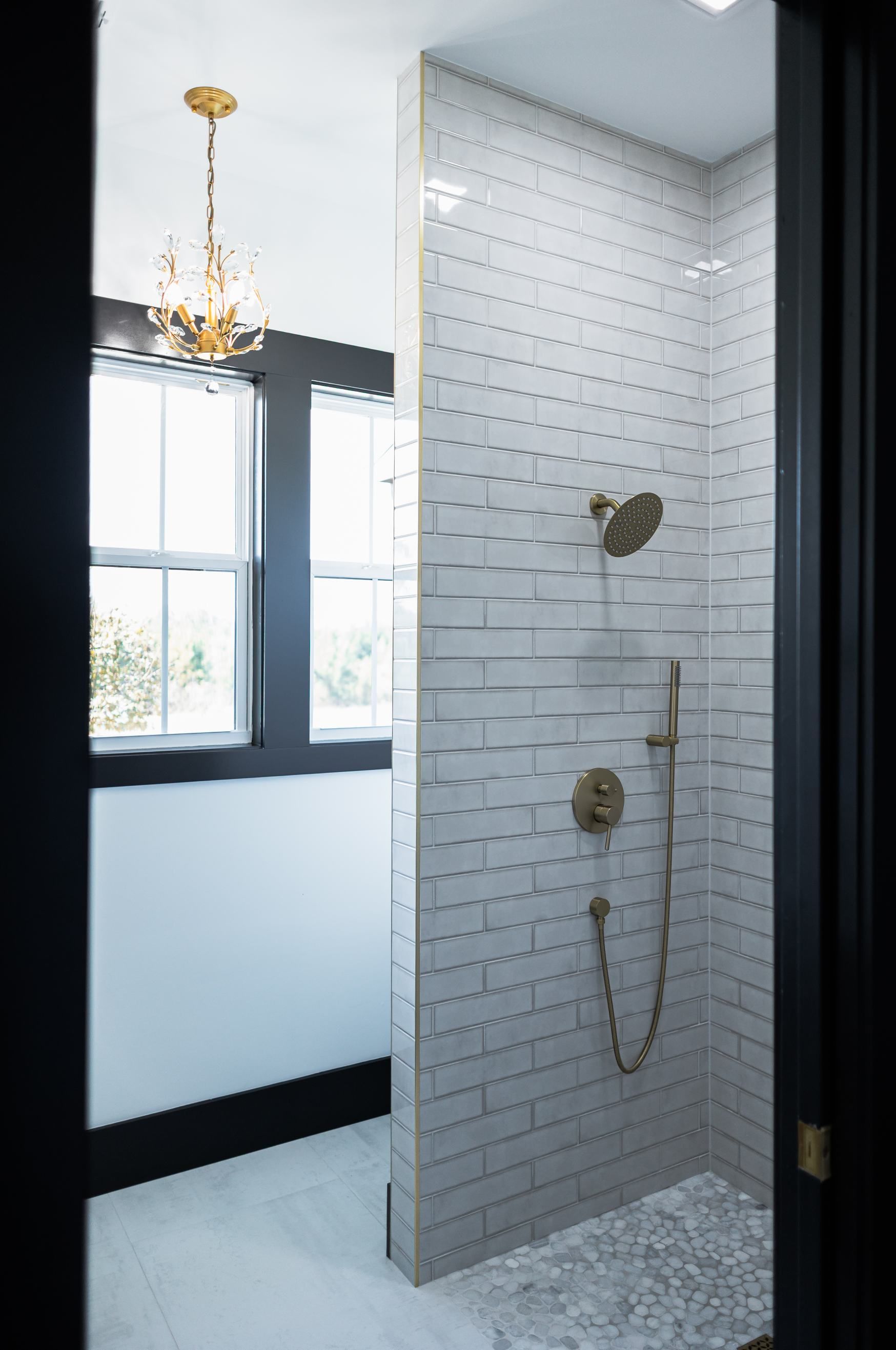 White-tiled shower with gold fixtures in a bright bathroom.