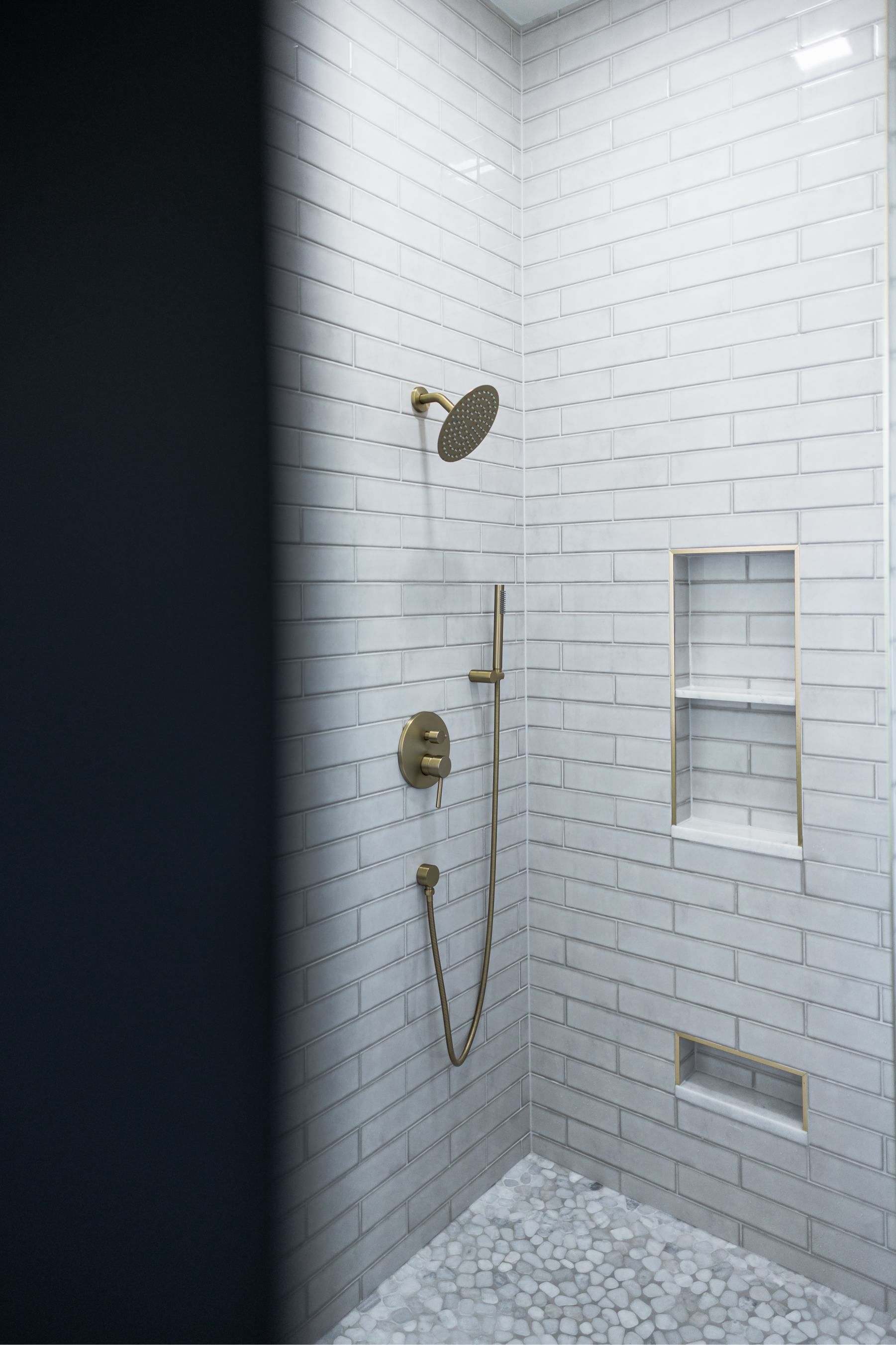 White tiled shower stall with gold fixtures, wall niches, and a handheld showerhead.