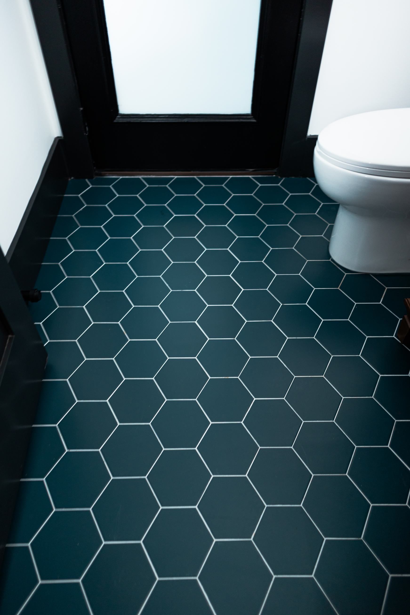 Small bathroom with dark hexagon tile floor, white walls, and a toilet on the right.