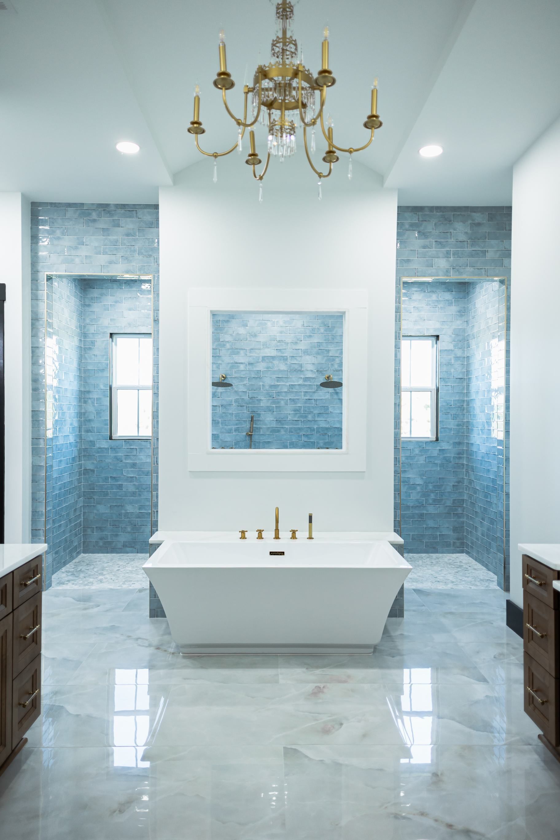 Luxurious bathroom with white bathtub, blue tile walls, marble floor, and gold chandelier