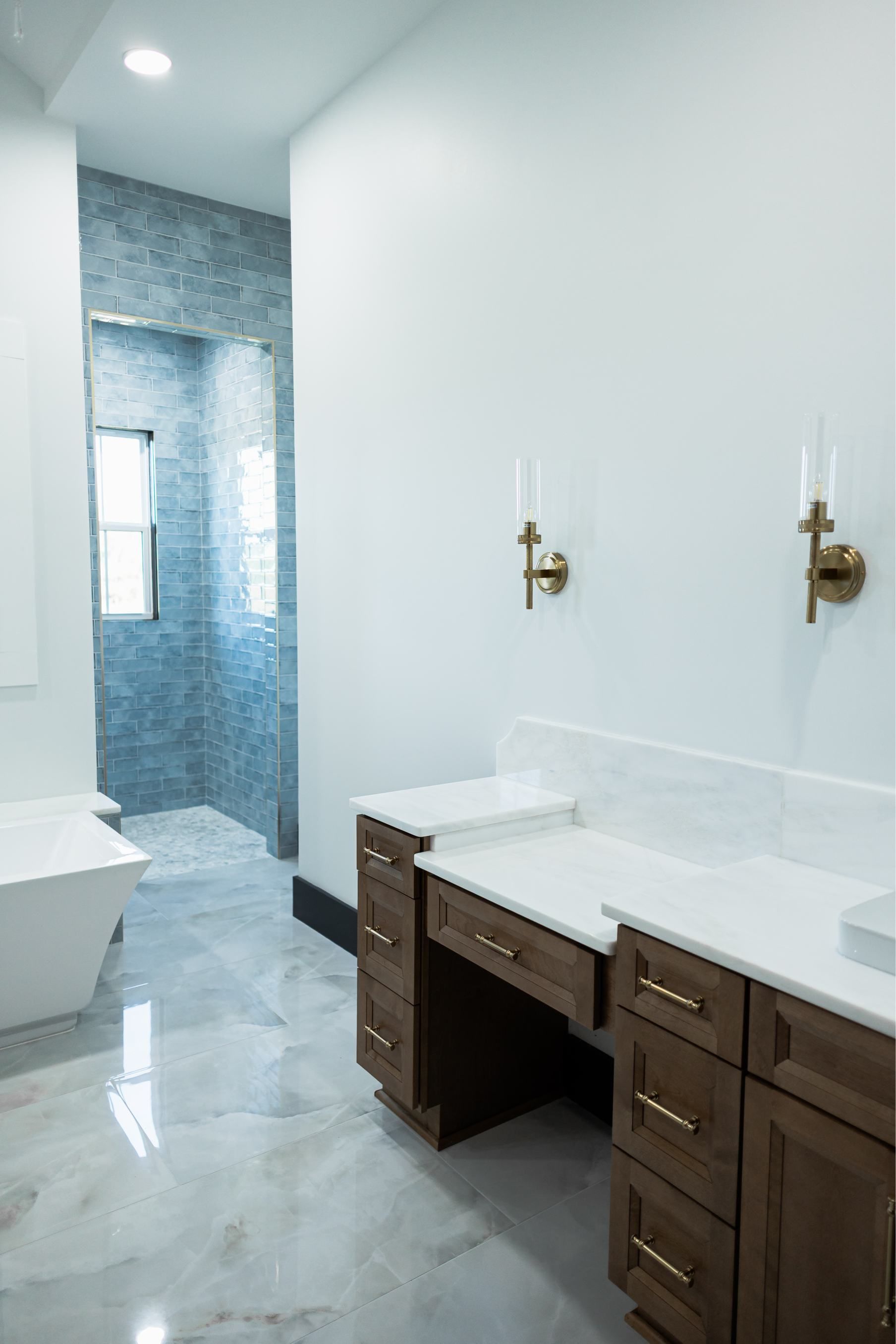 Modern bathroom with white marble vanity, brass sconces, and blue-tiled shower area
