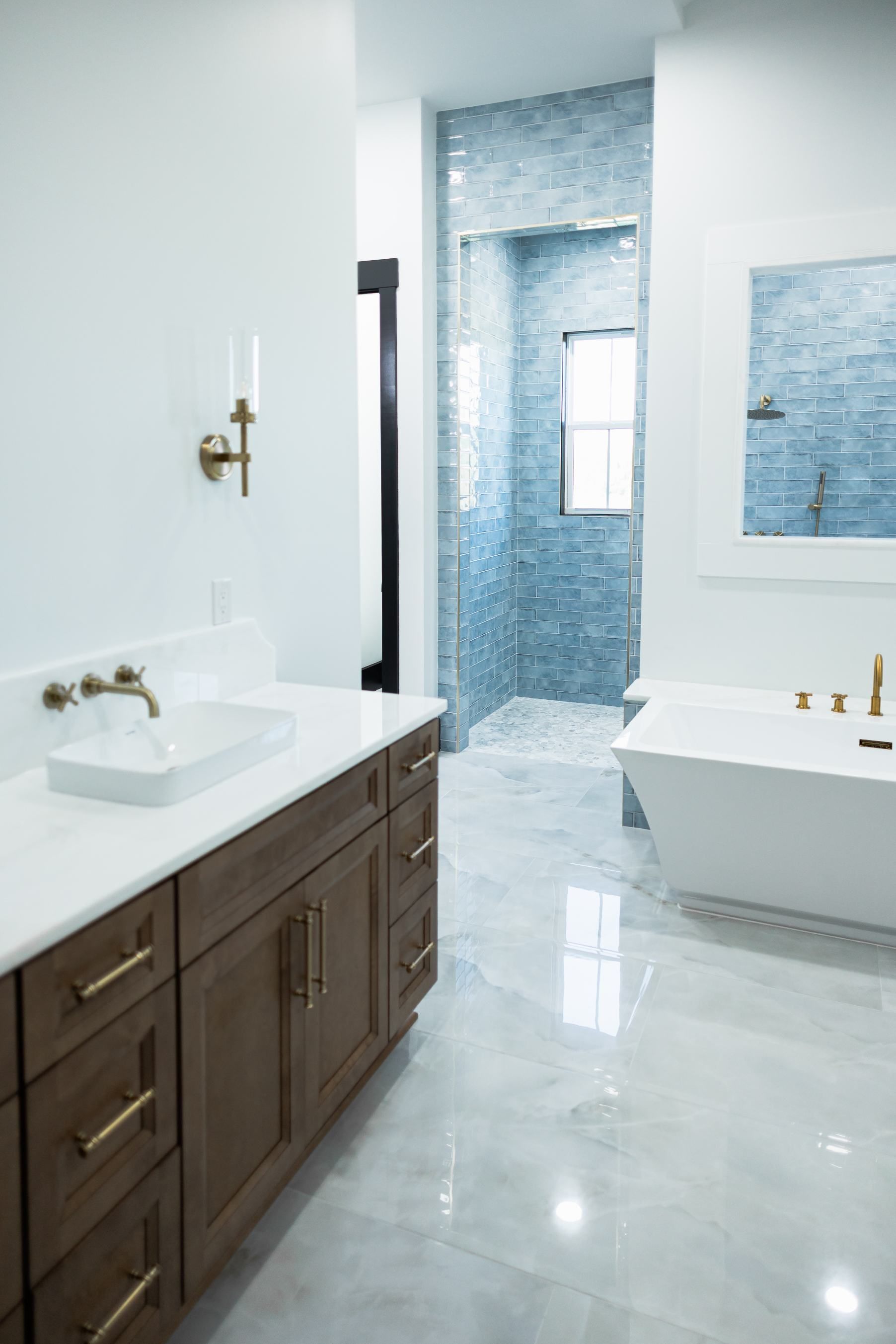 Bright modern bathroom with double vanity, white tub, and blue tile shower.