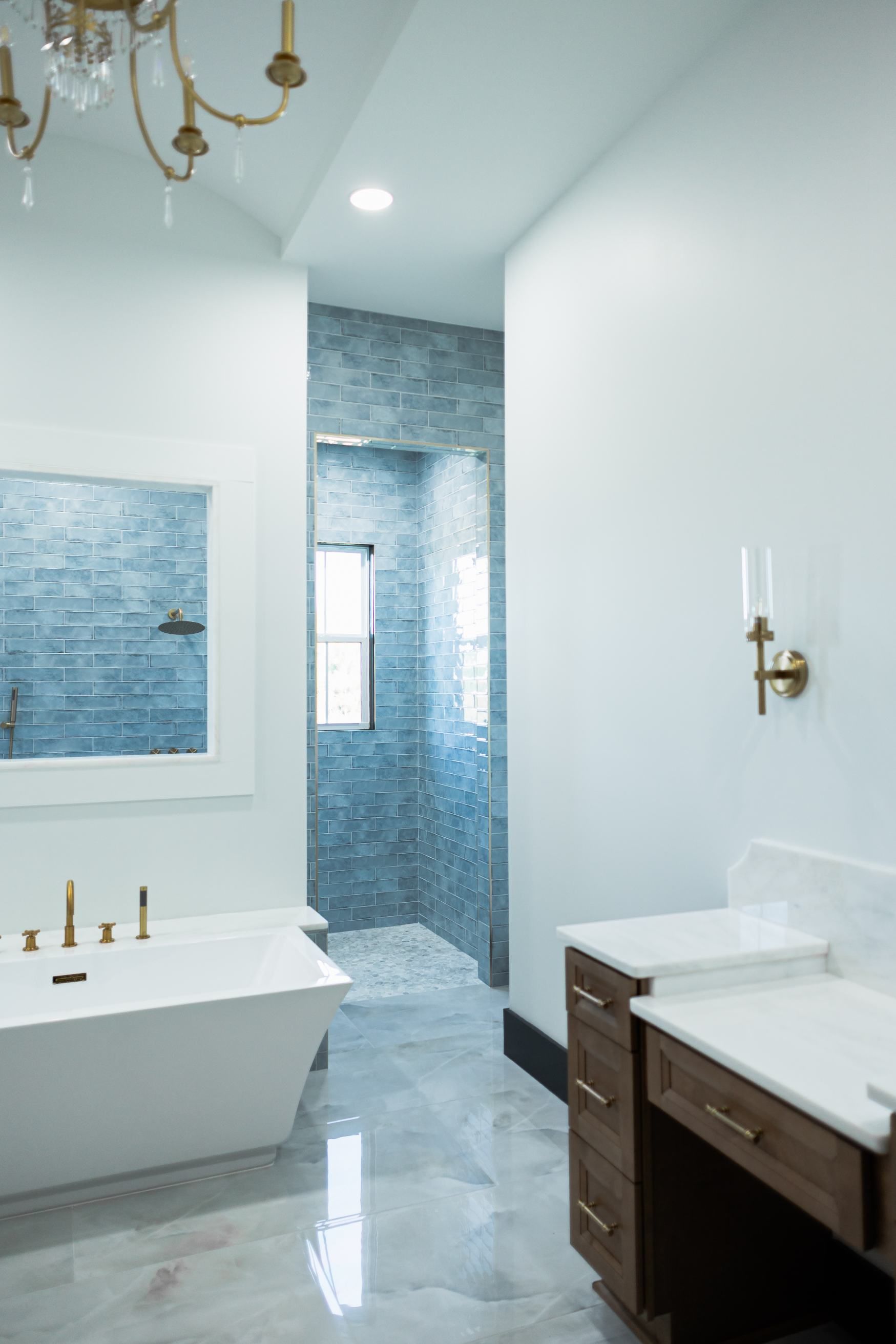 Bright bathroom with white tub, dark vanity, marble countertop, and blue-tiled shower alcove.
