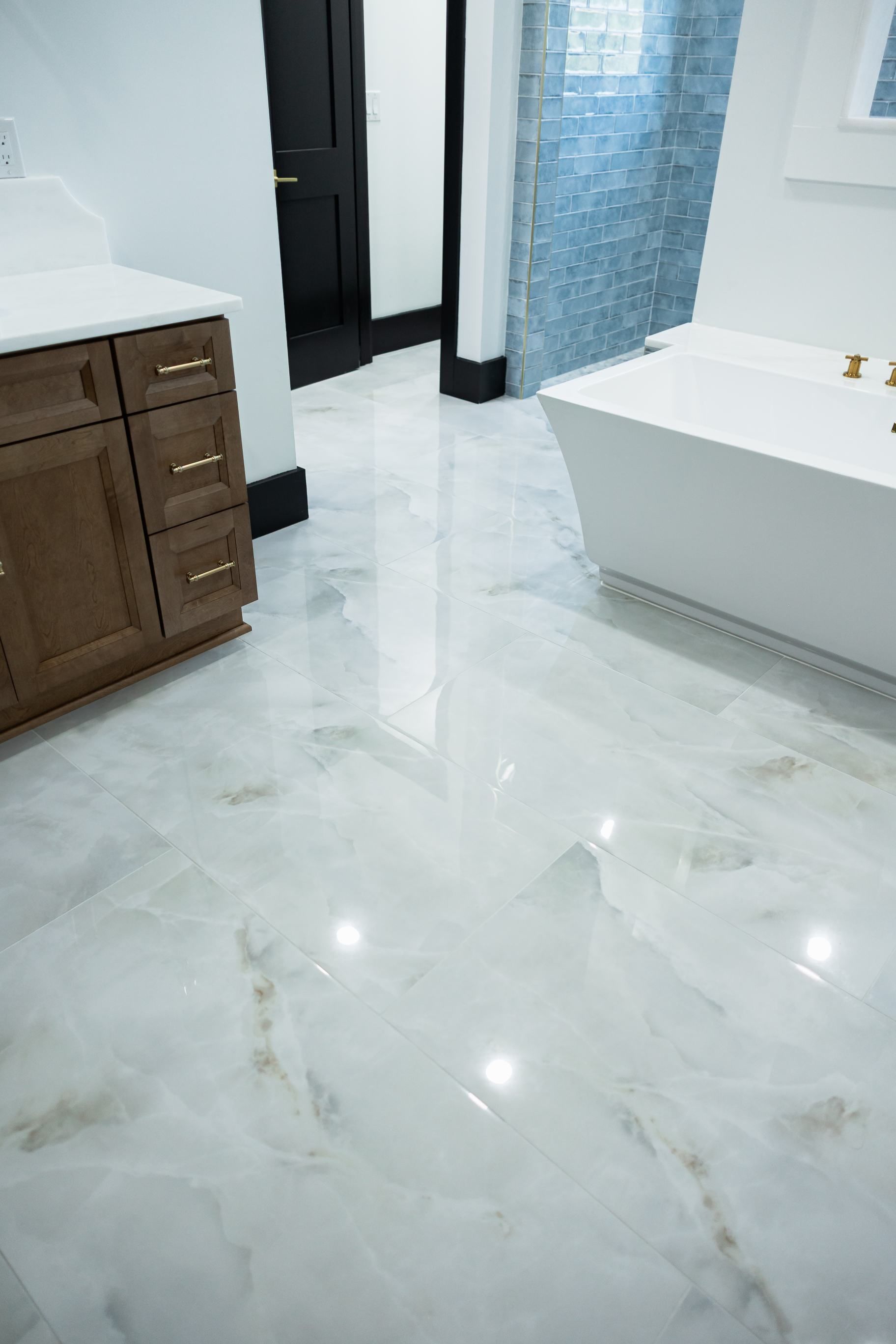 Bright marble bathroom floor with a wooden vanity, toilet, shower curtain, and white bathtub.
