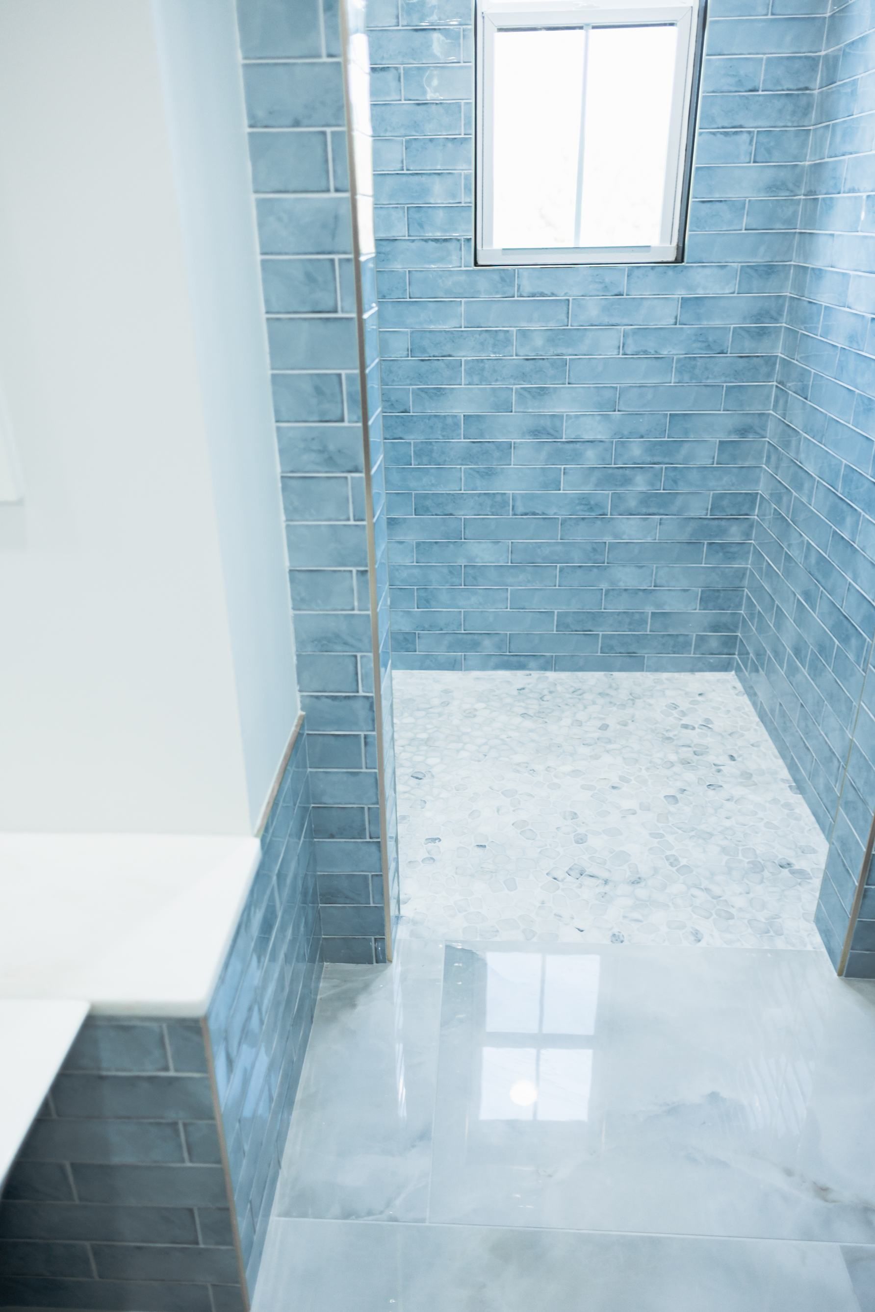 Blue-tiled shower stall with a window and white floor tiles