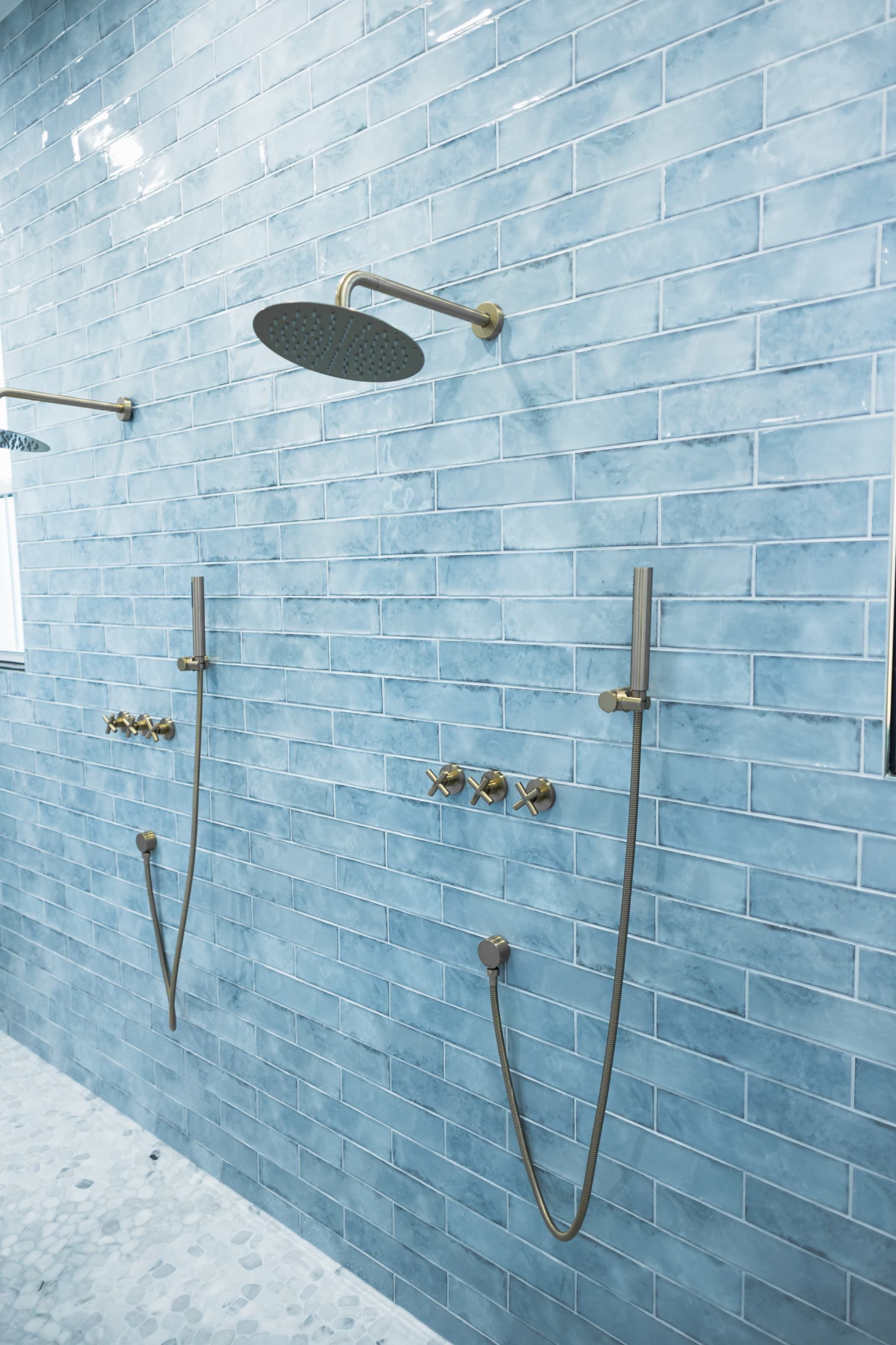 Blue tiled shower wall with two showerheads and chrome fixtures