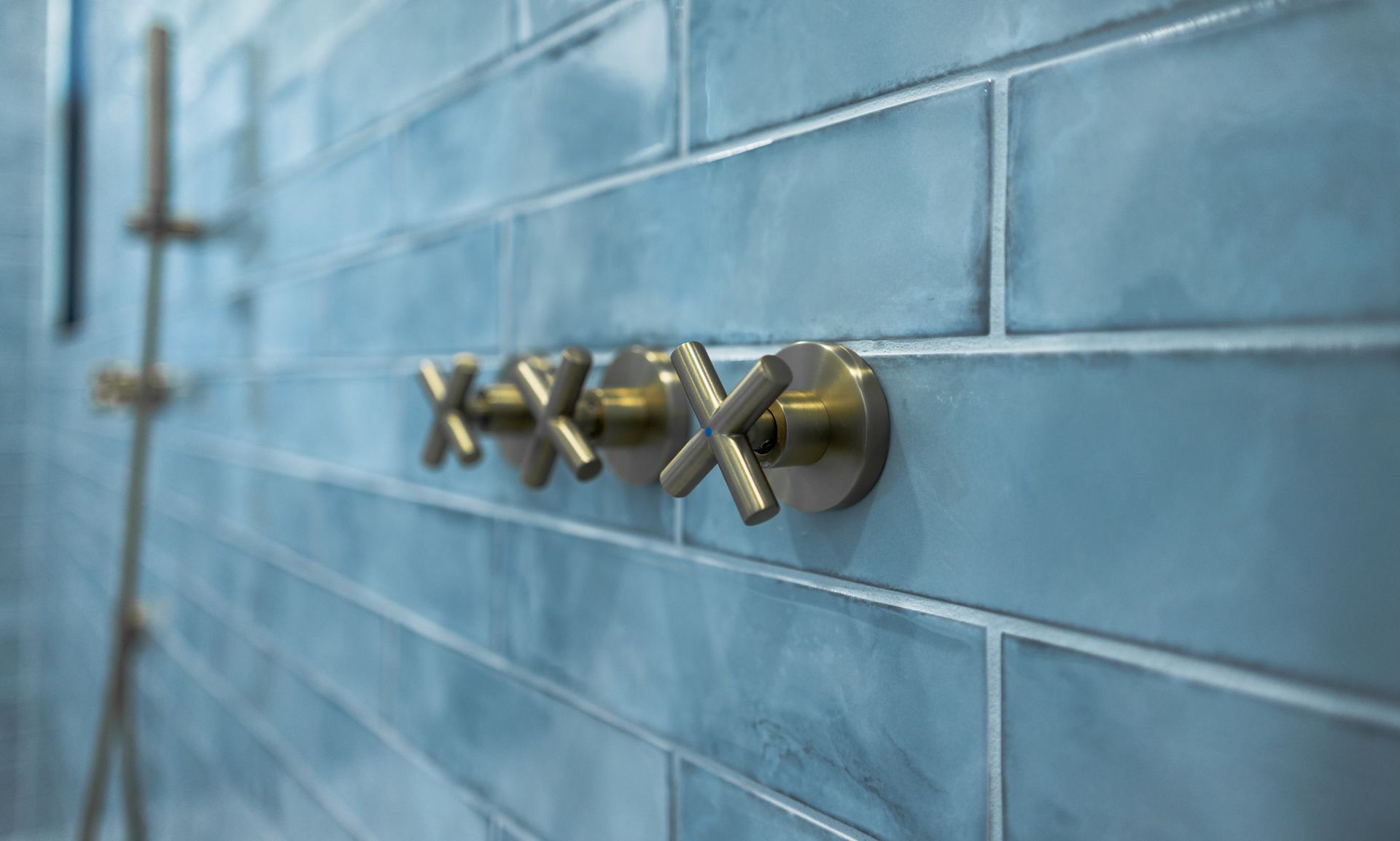 Brass cross handles mounted on blue tiled shower wall