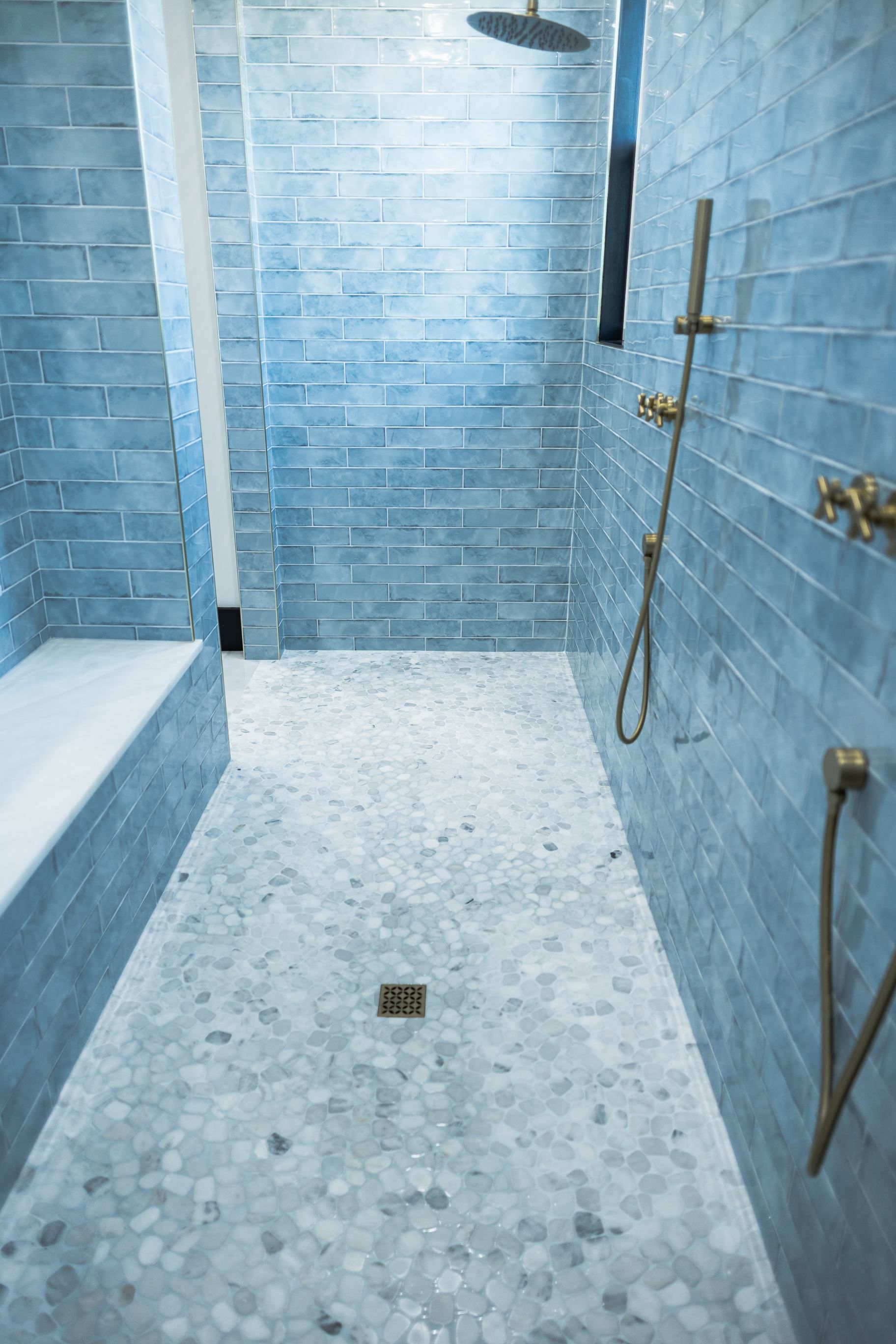 Blue-tiled shower stall with mosaic floor, glass door, and gold fixtures