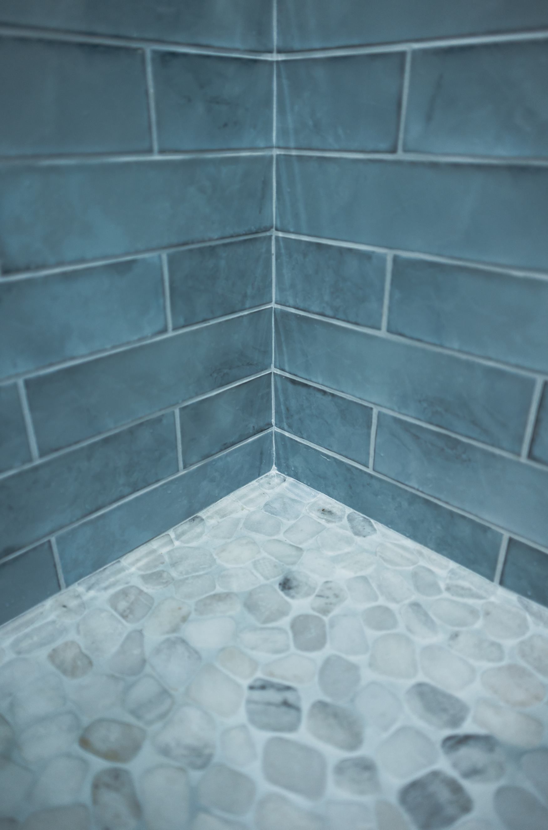 Corner of a blue-tiled shower with a pebble stone floor.