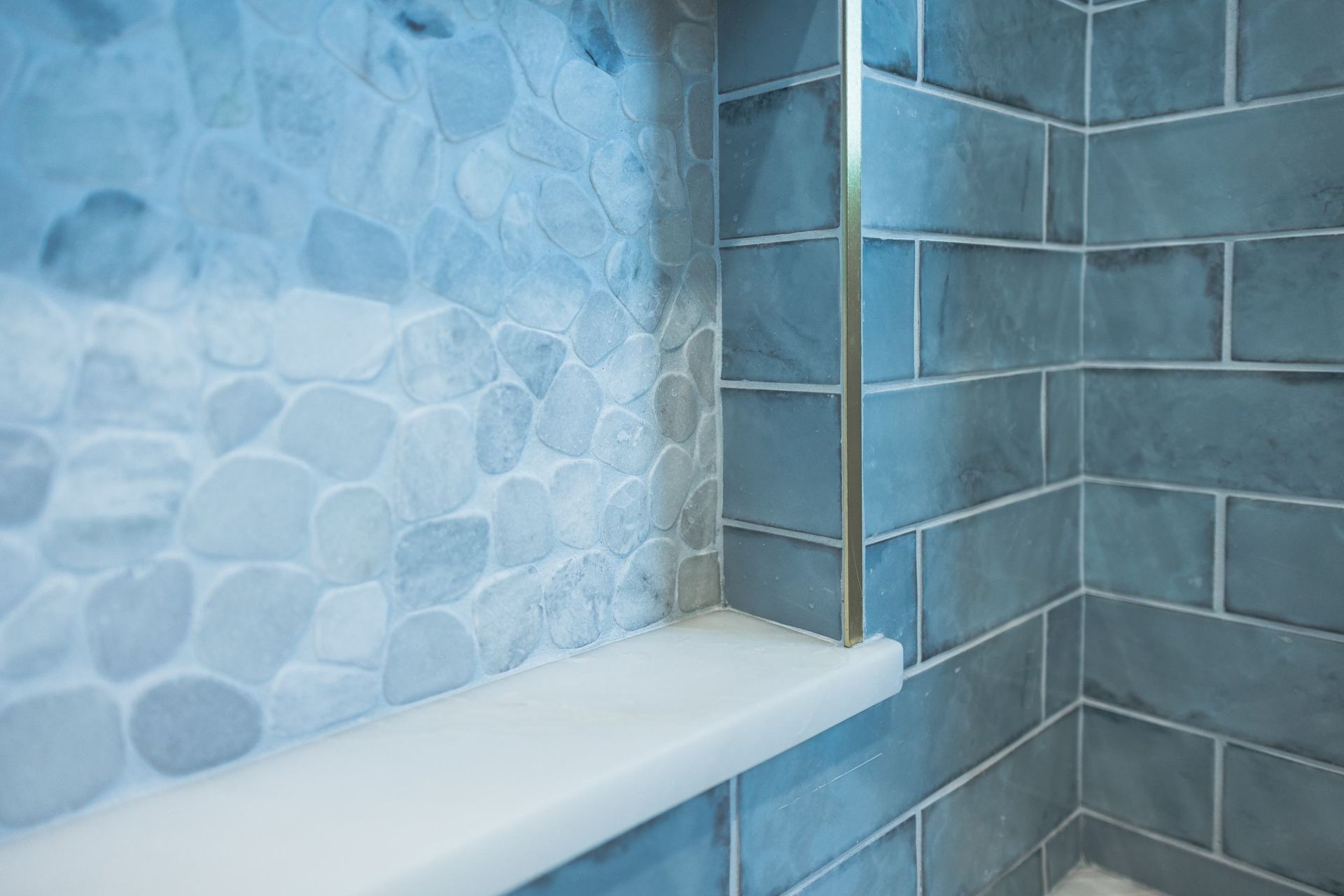 Blue tiled shower corner with stone-patterned wall and a white shelf