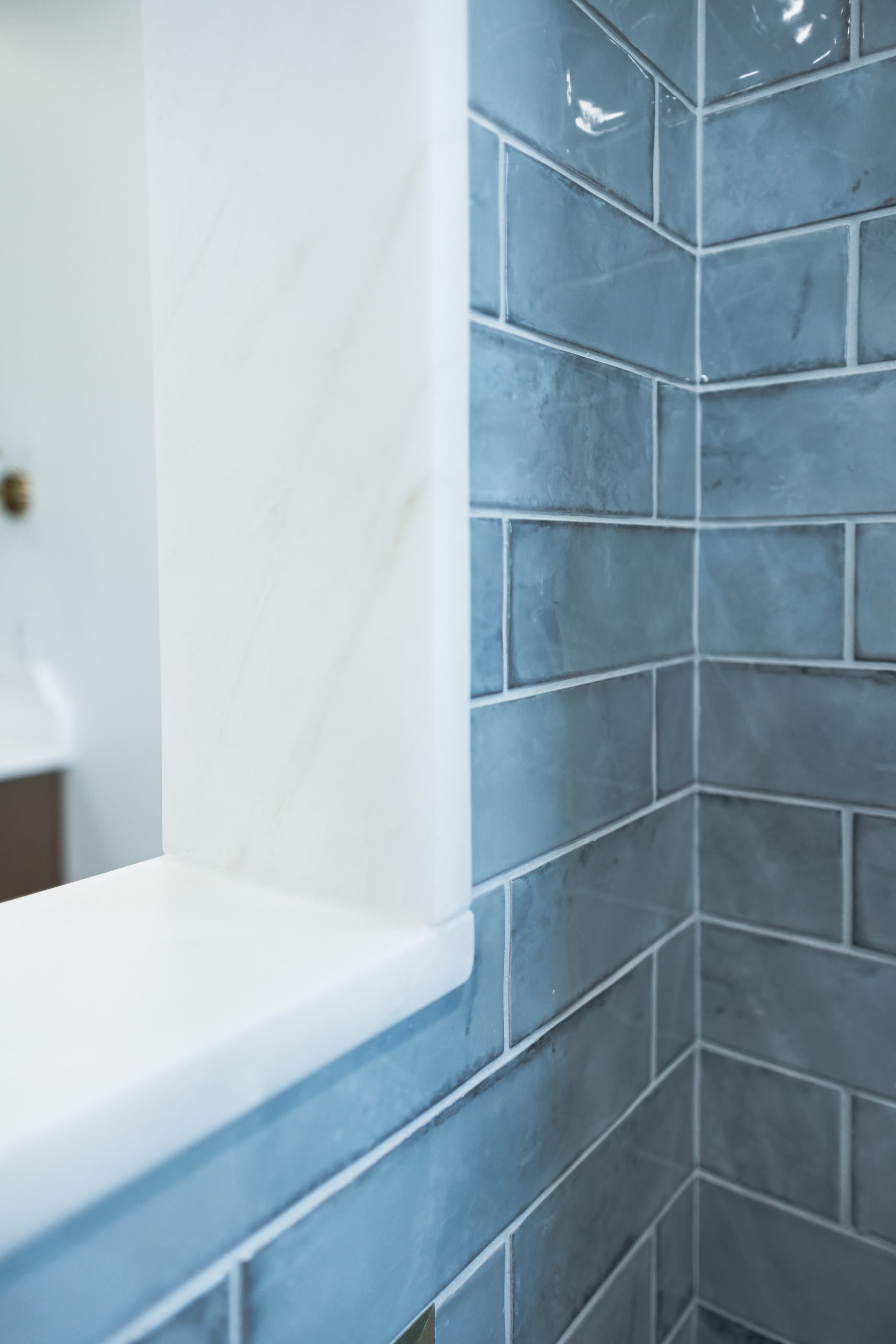 Blue tiled bathroom shower wall with white ledge and mirror edge