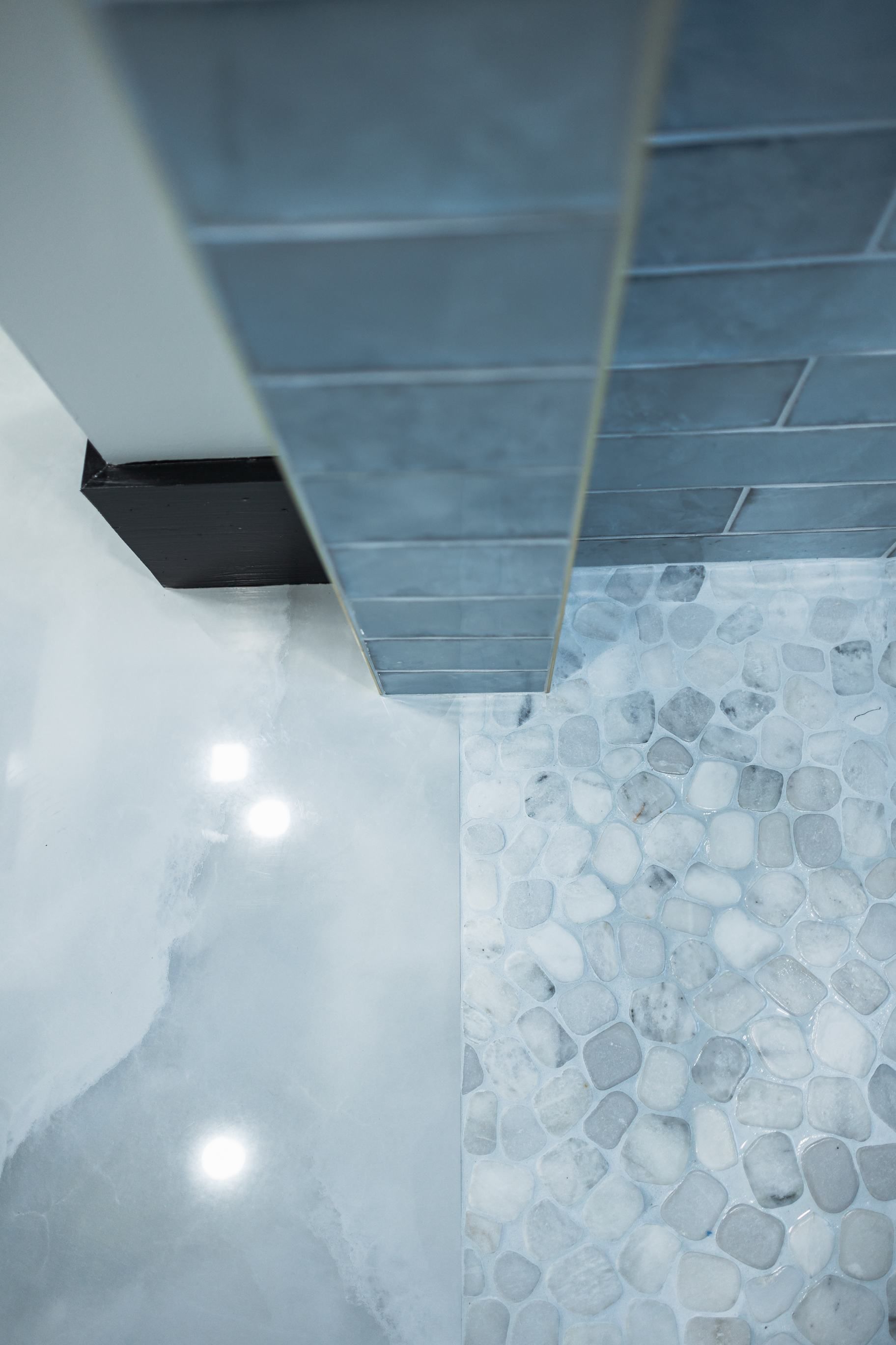 Bathroom corner with gray tile wall, white floor, and pebble-pattern shower base at right