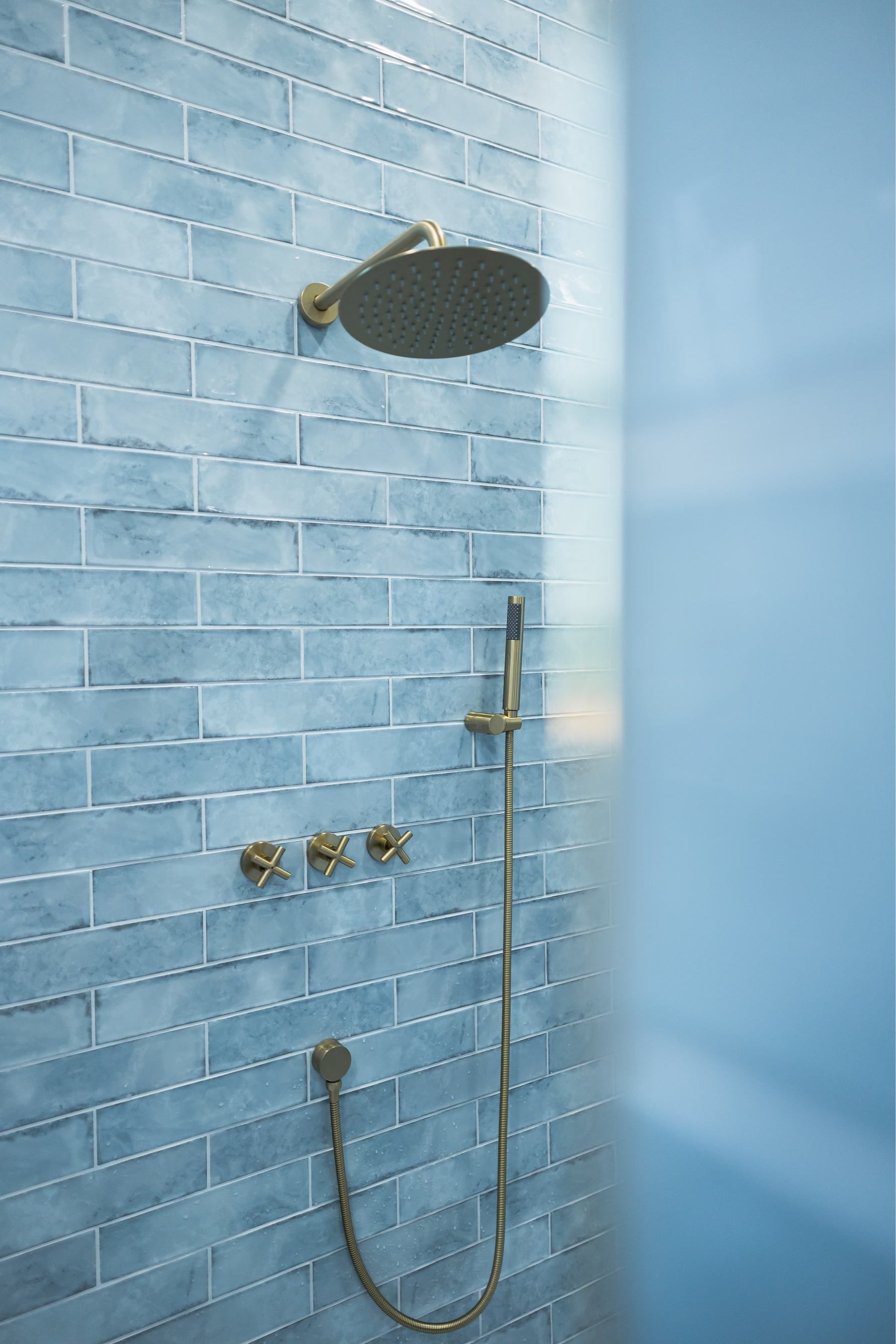 Blue-tiled shower with round rainfall head, handheld sprayer, and hose against a light blue wall.